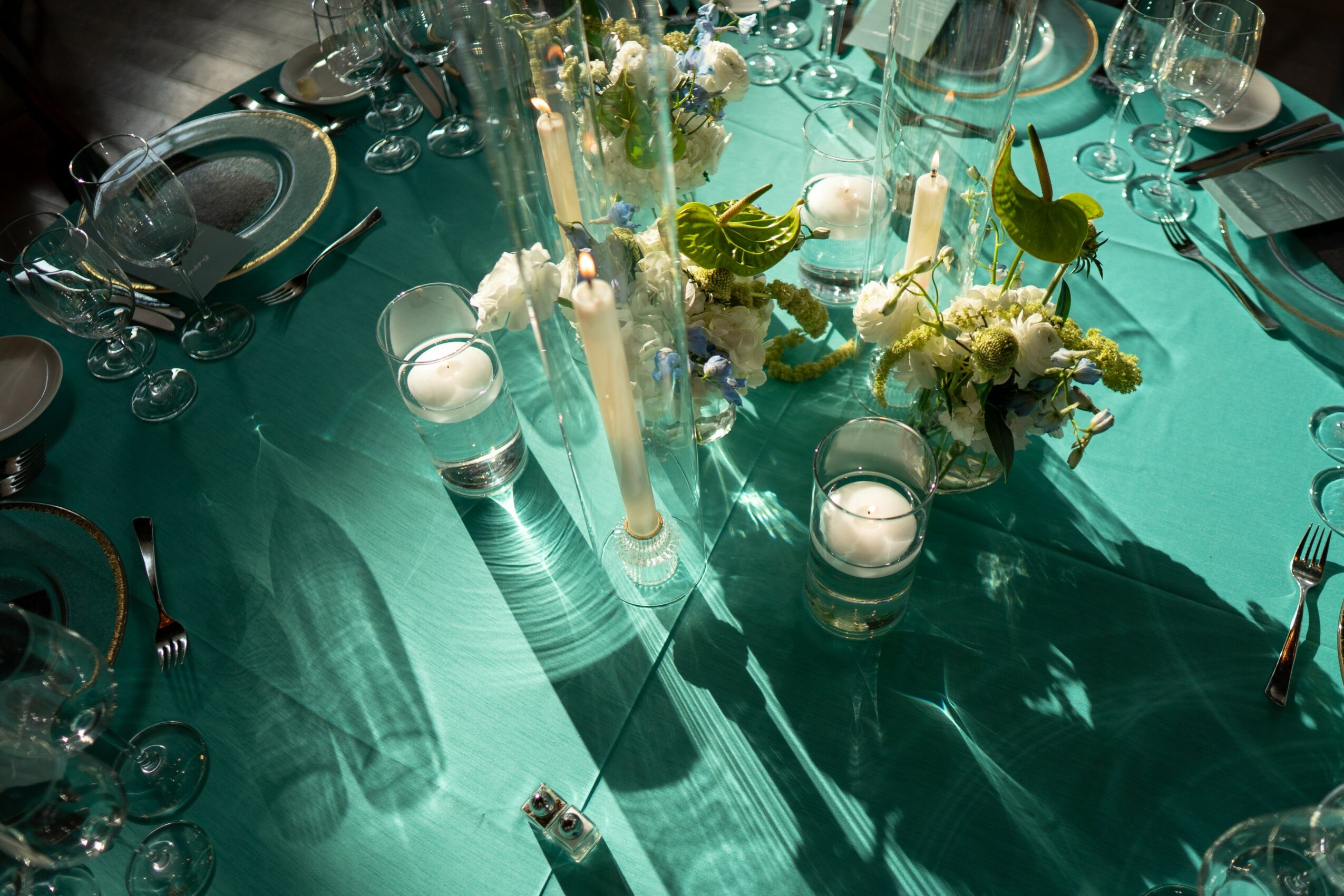 Table with floral centerpiece, candles, glassware, and tableware on a teal tablecloth.