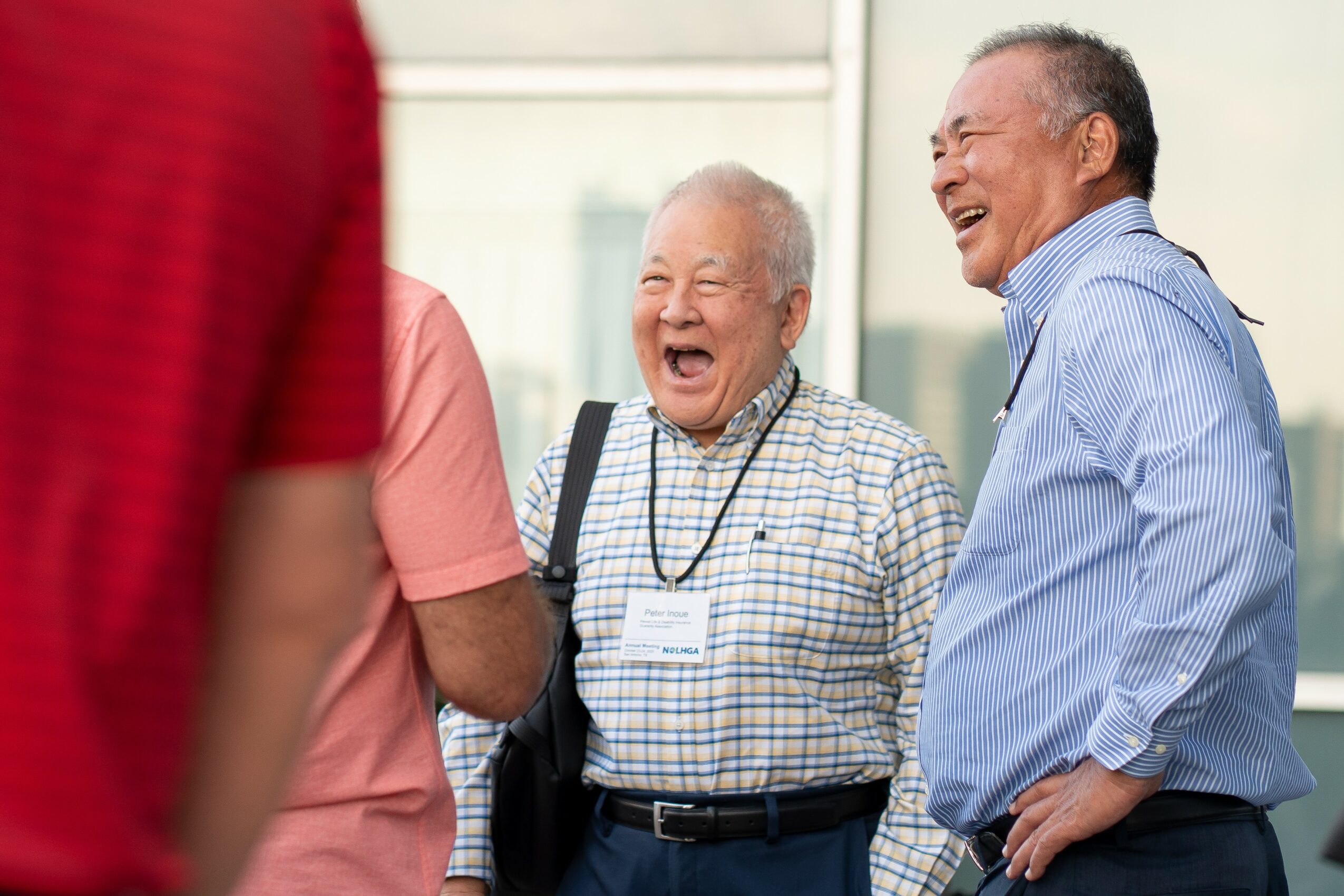 Three people laughing and talking indoors, with a window in the background.