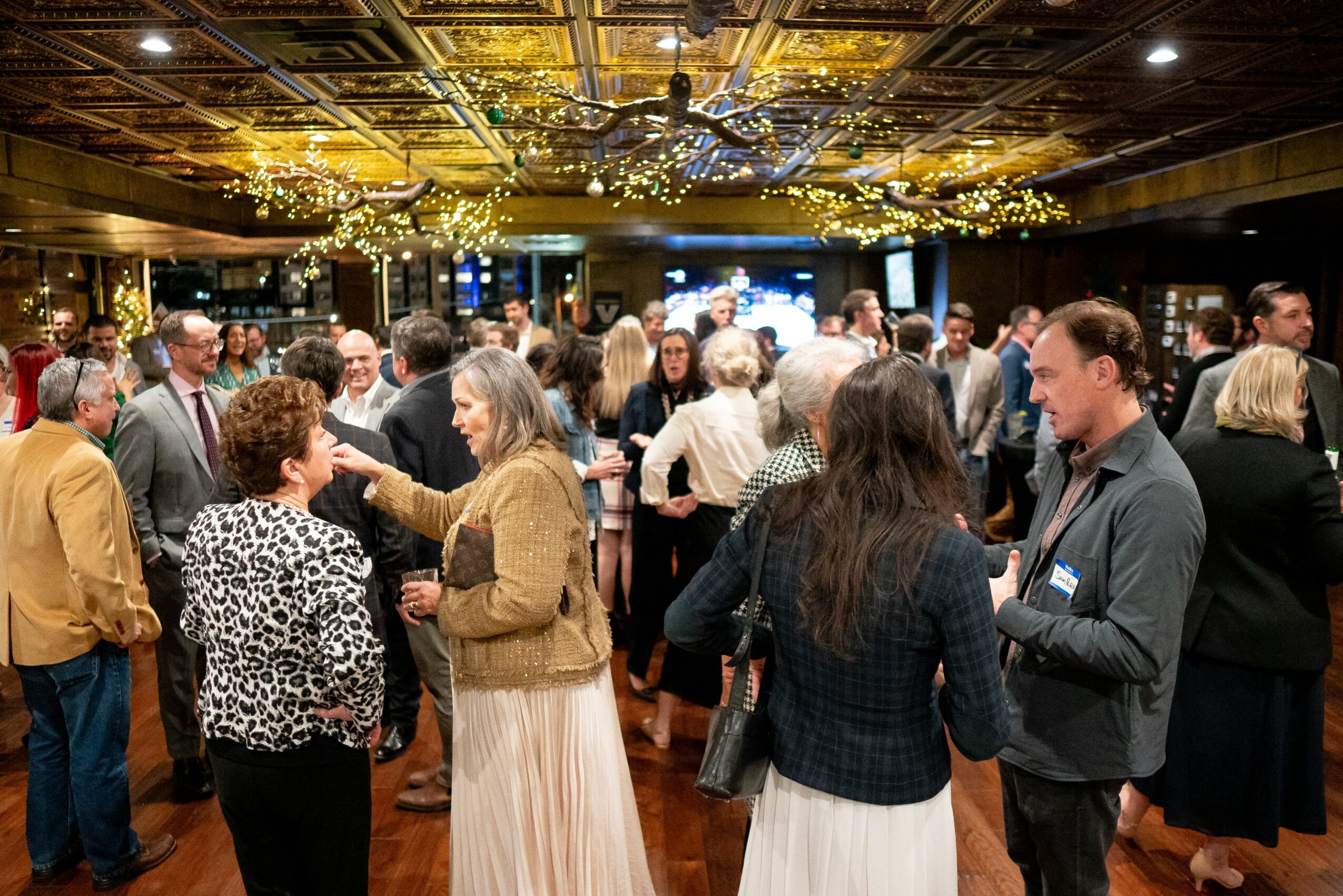 People socializing in a decorated banquet hall with a chandelier ceiling and a stage in the background.