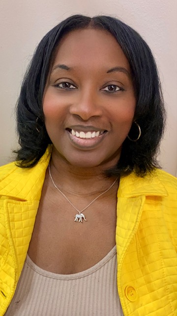 Woman with shoulder-length black hair, wearing a yellow jacket and a necklace with an elephant pendant.