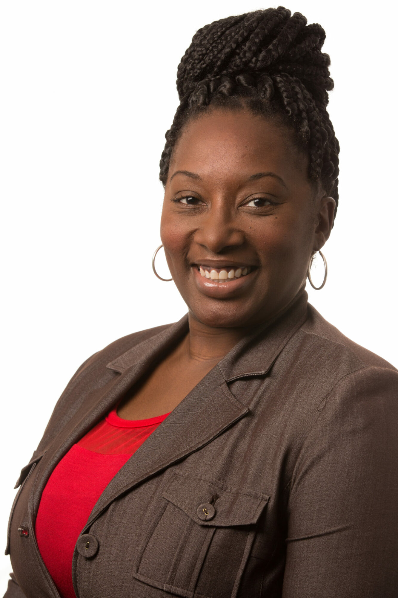 Woman with braided hair smiling, wearing a brown blazer and red top, against a white background.