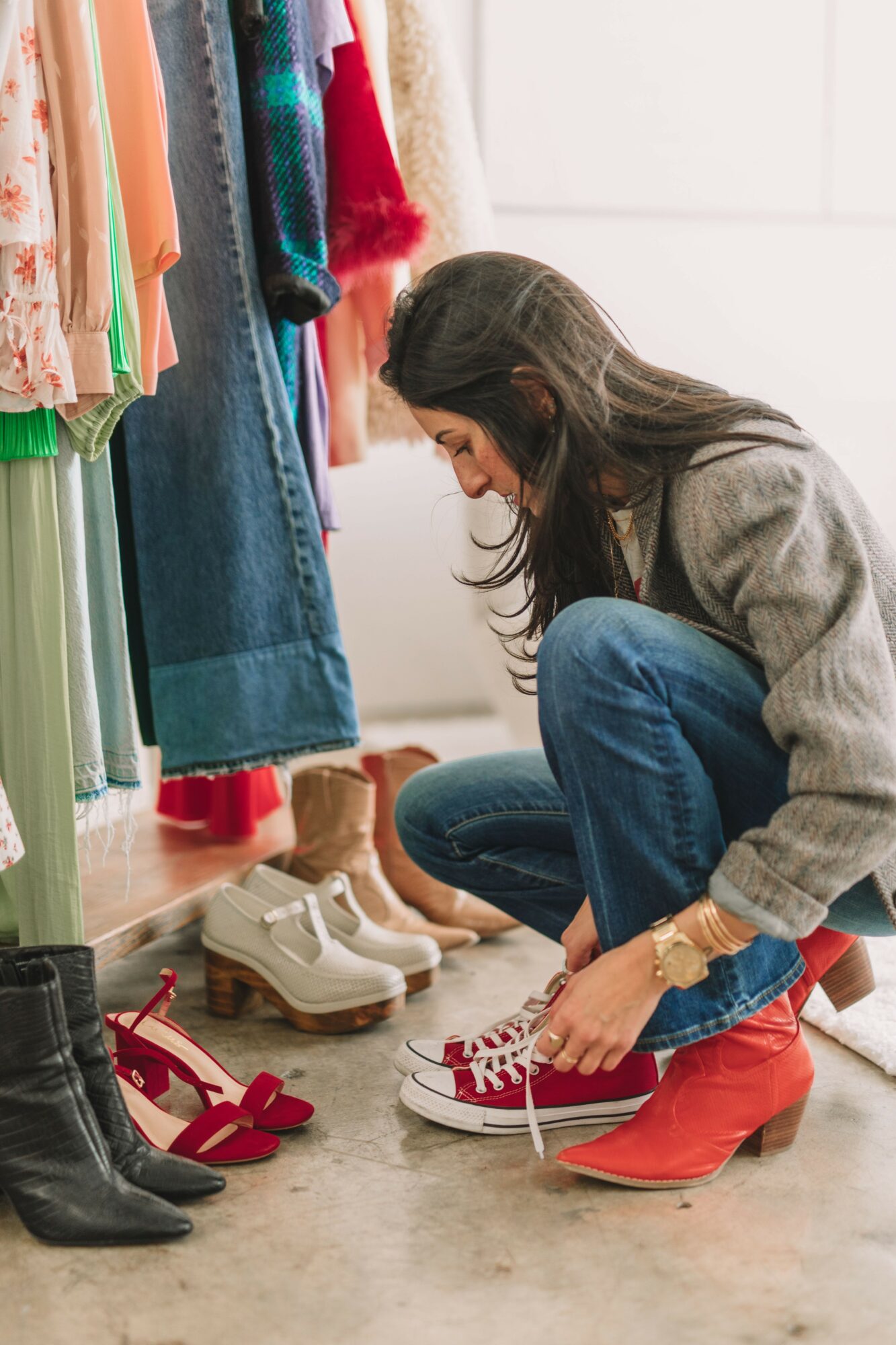 Woman trying on red sneakers in a clothing store, surrounded by shoes and hanging clothes.