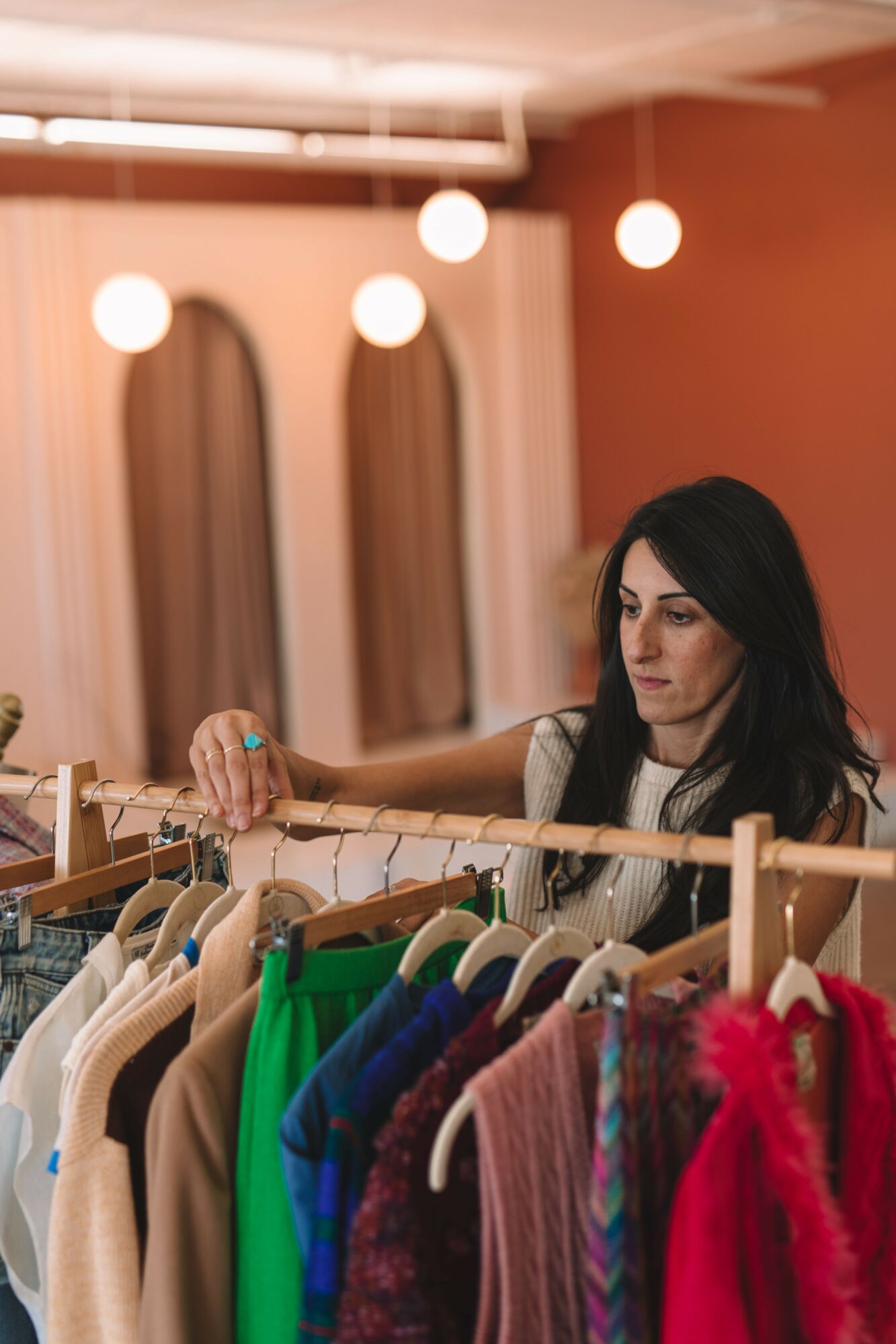 Woman with dark hair shopping for colorful clothes on a rack inside a store.