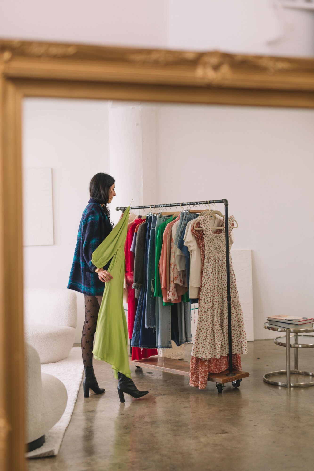 Person browsing colorful clothes on a rack in a minimalist room with white walls and concrete floor.