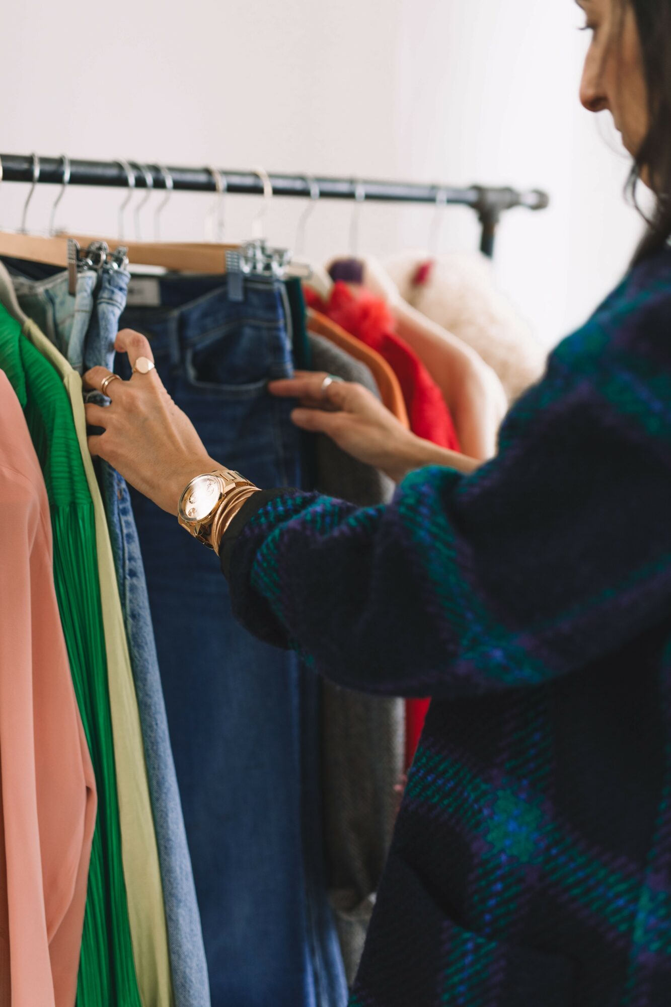 Person shopping for clothes, holding a pair of jeans and examining garments on a rack.