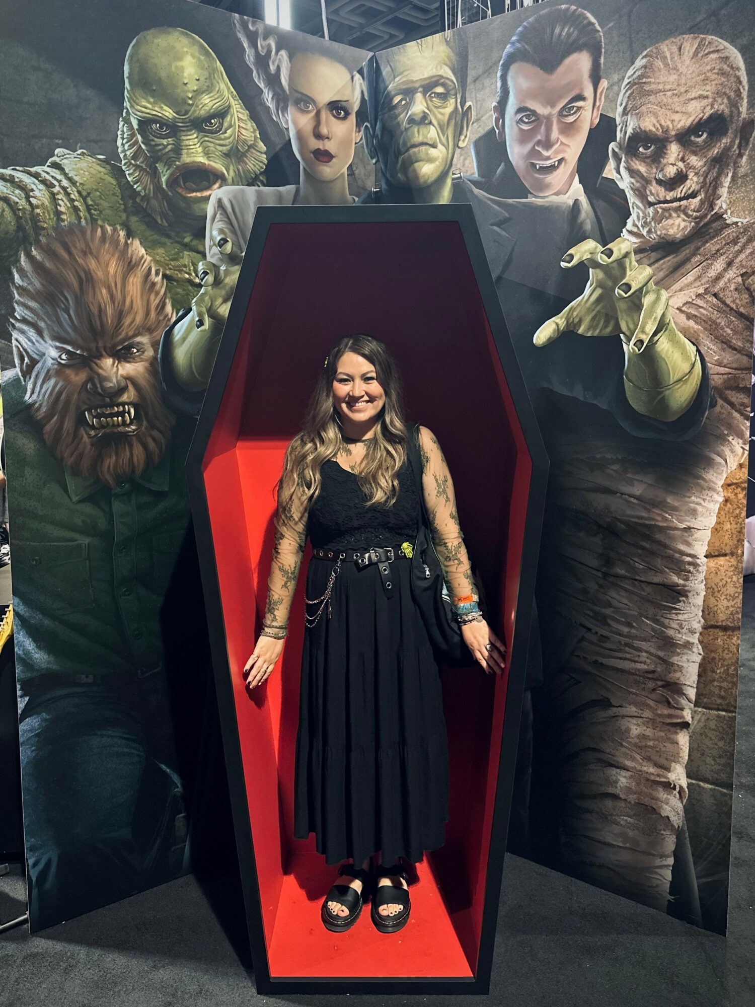 Woman standing inside a coffin-shaped display with fantasy characters painted on the background wall.