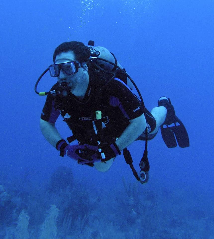 Person scuba diving underwater wearing a mask, snorkel, wetsuit, and fins, with a diving tank and equipment.