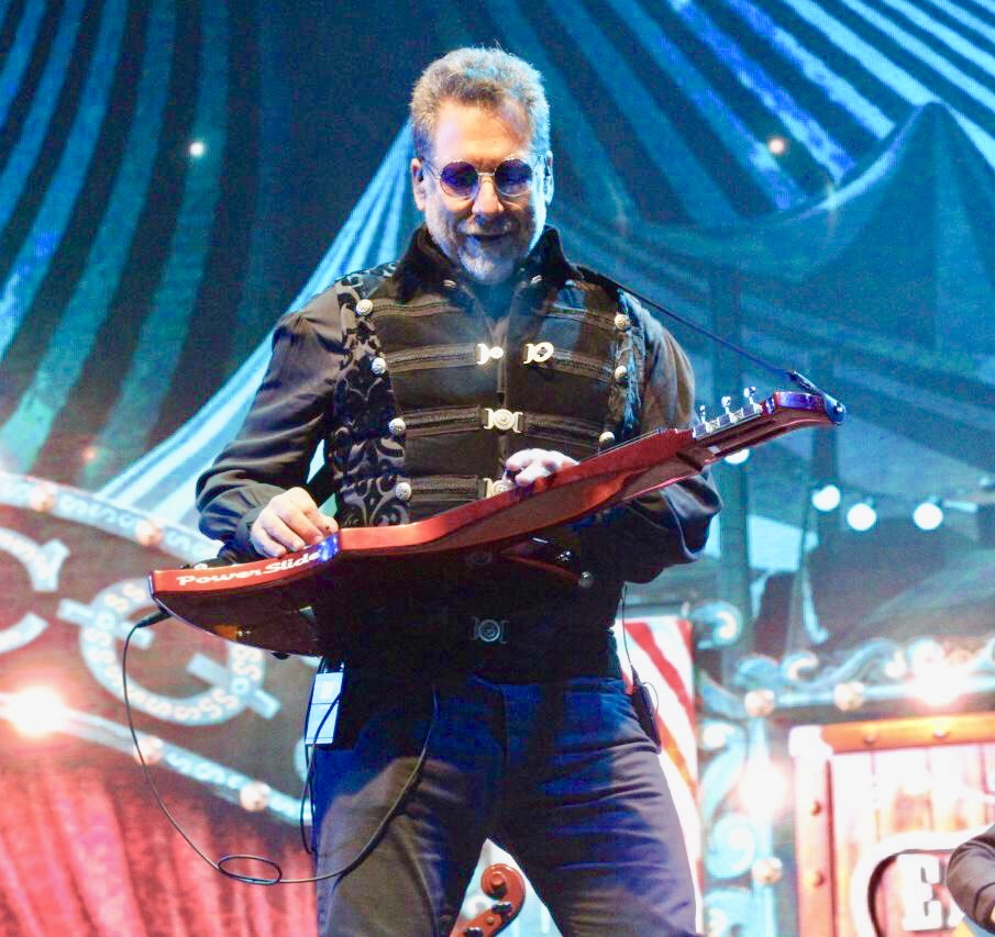 Man playing a guitar on stage with colorful background and lighting effects.