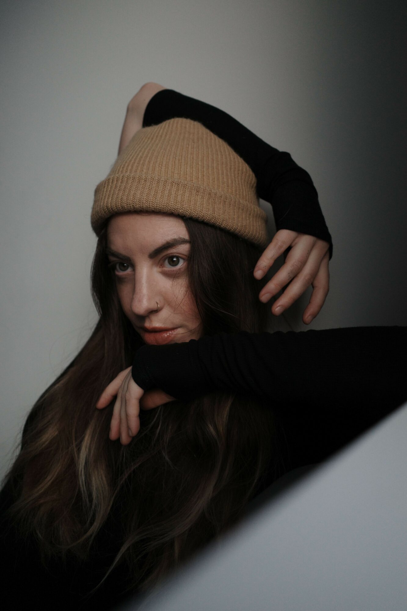 Young woman wearing a tan beanie and black gloves, resting her head on her hand, looking to the side.