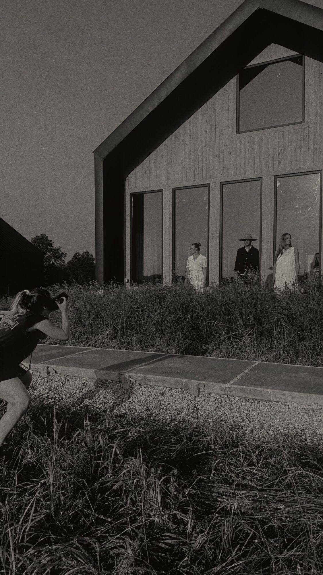 Person crouching on grass taking a photo of four people standing in front of a building.
