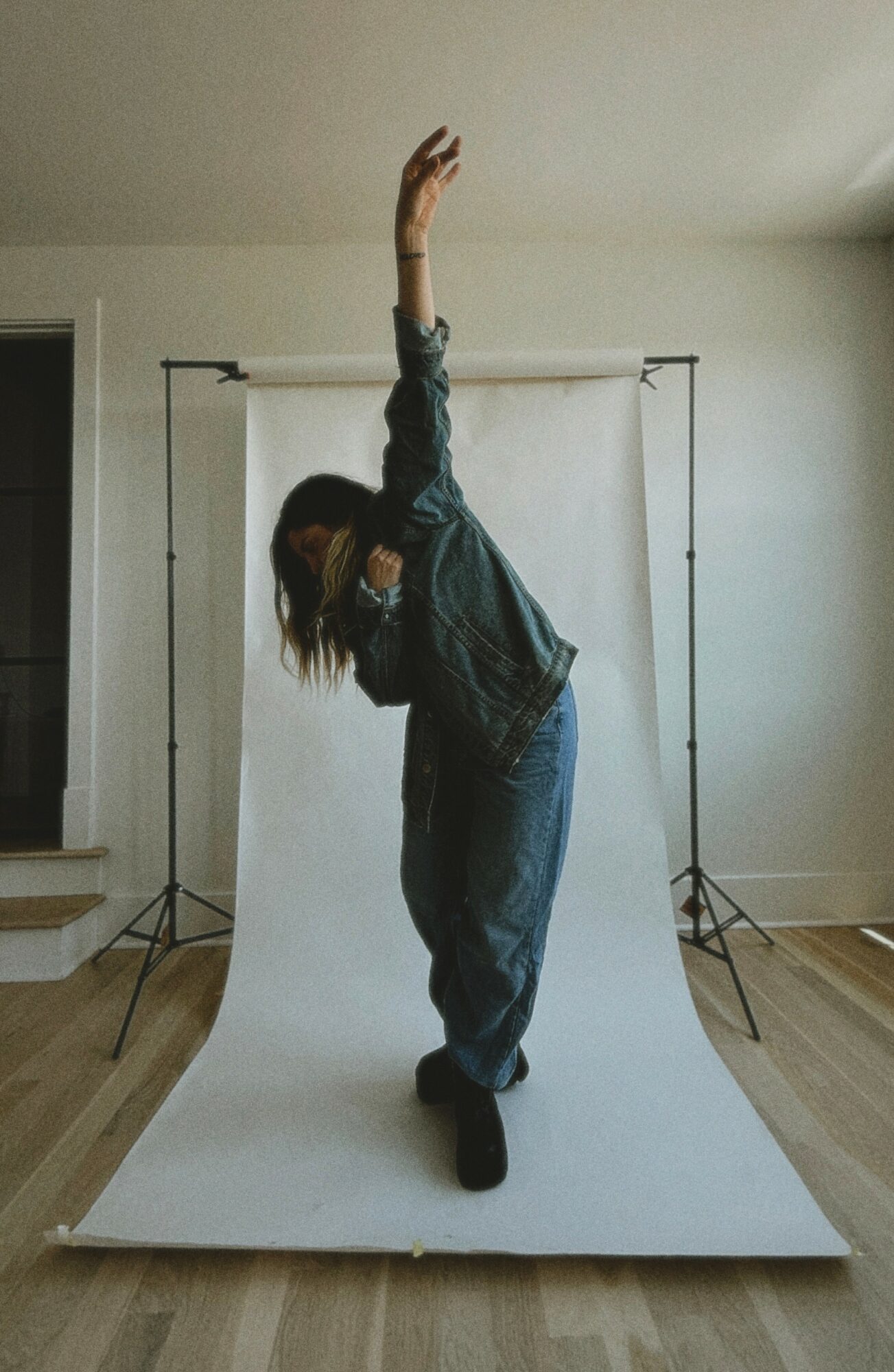 Person bending sideways with one arm raised, standing on a white backdrop in a room.