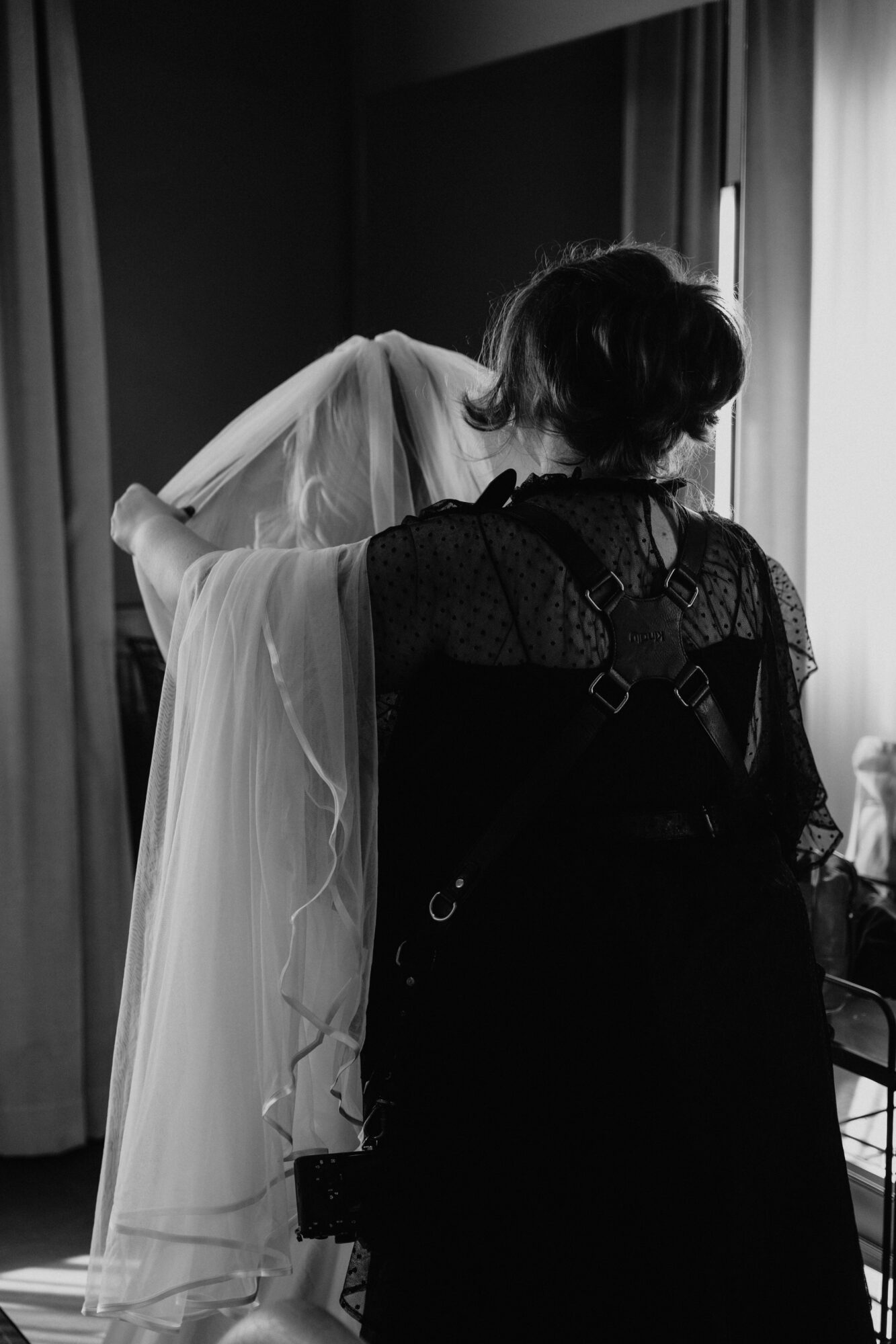 Two women with short hair, one in a light dress, the other in dark clothing, standing near a window.
