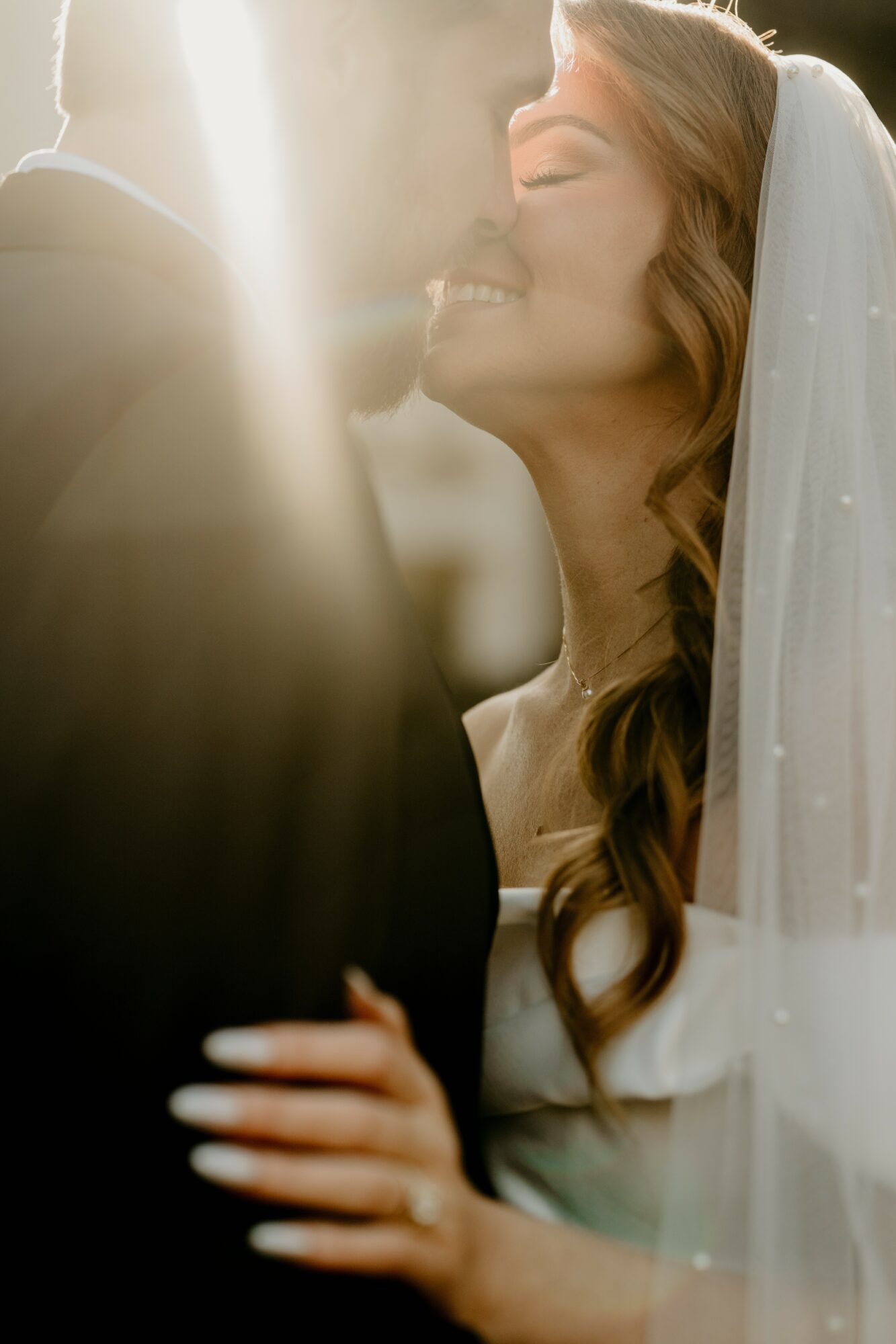 A bride and groom close together, smiling, with sunlight behind them, in a wedding scene.