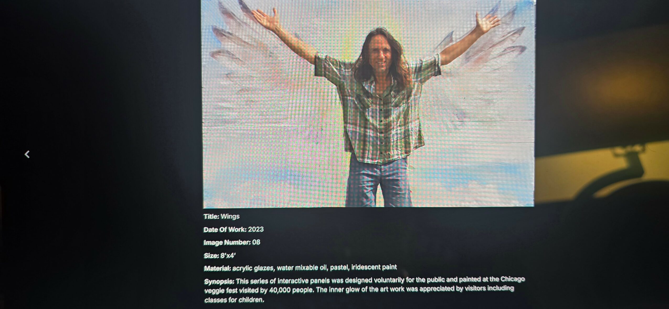 Person with long hair and plaid shirt standing with arms outstretched in front of a bright background.