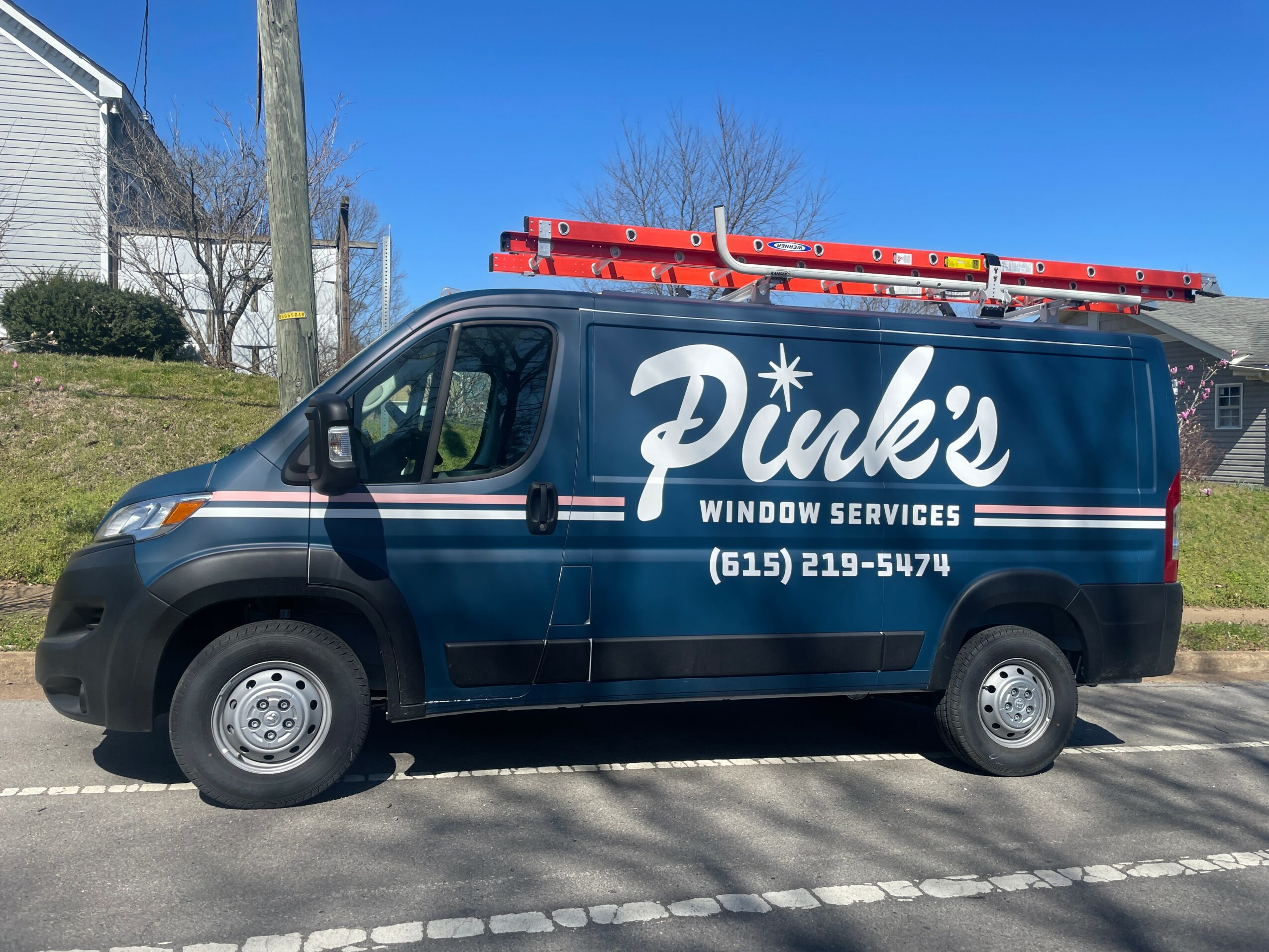 Dark blue van with white and red lettering, parked on a street, advertising Puke's Window Services, phone number visible.