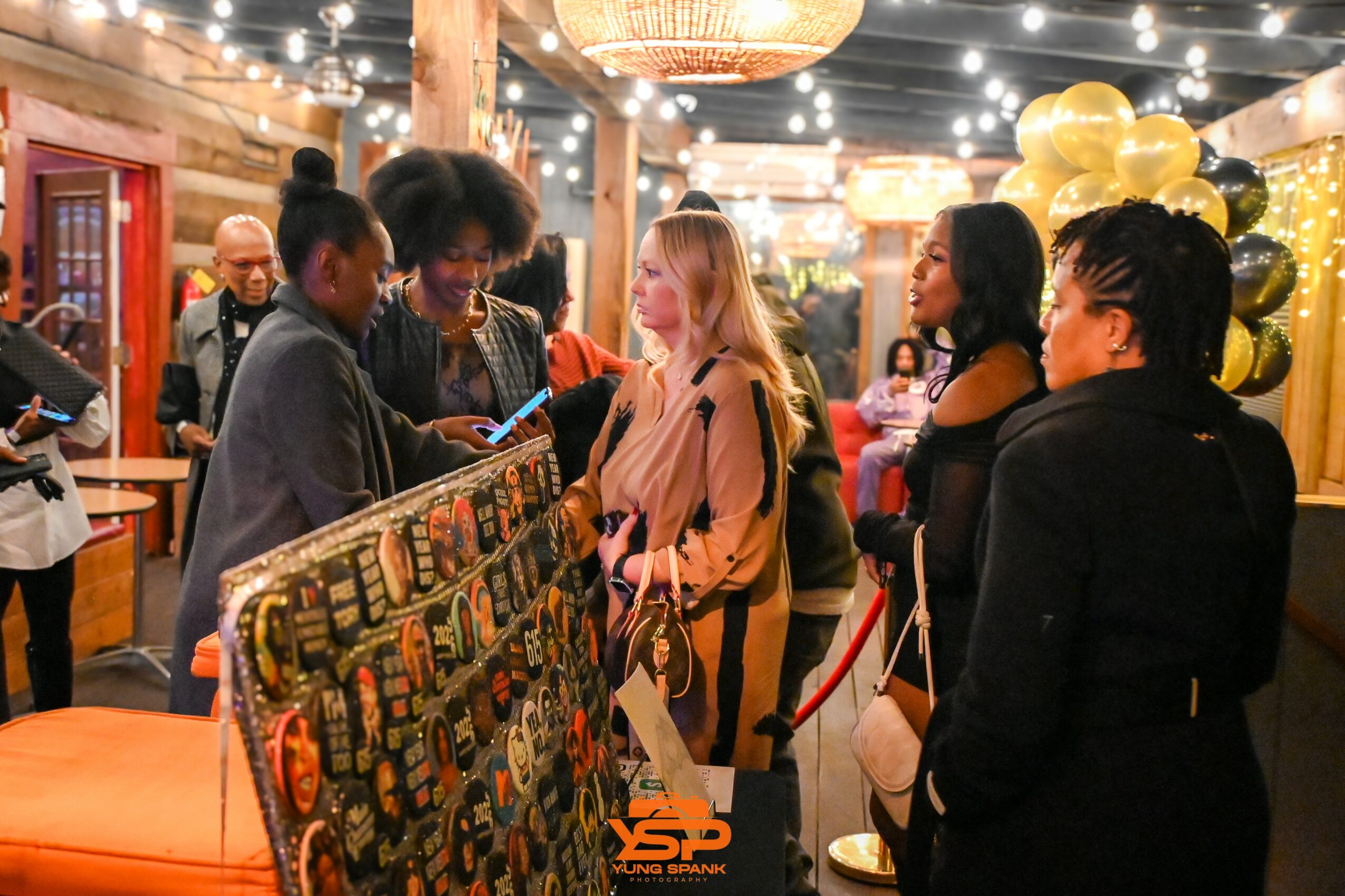Group of women standing in line at an indoor event, with balloons and string lights in the background.