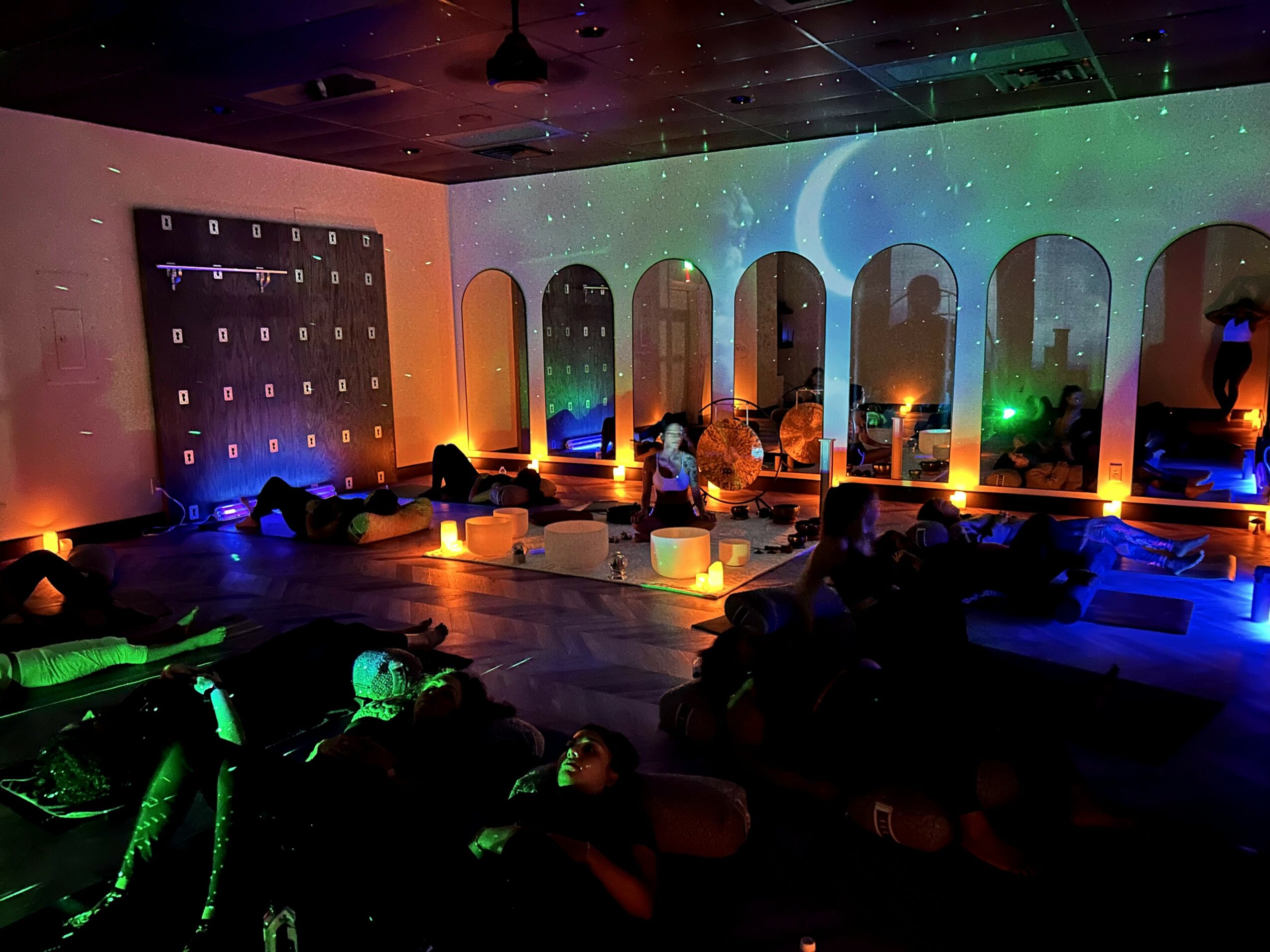 Indoor event space with colorful lighting, arched windows, and people sitting and relaxing.