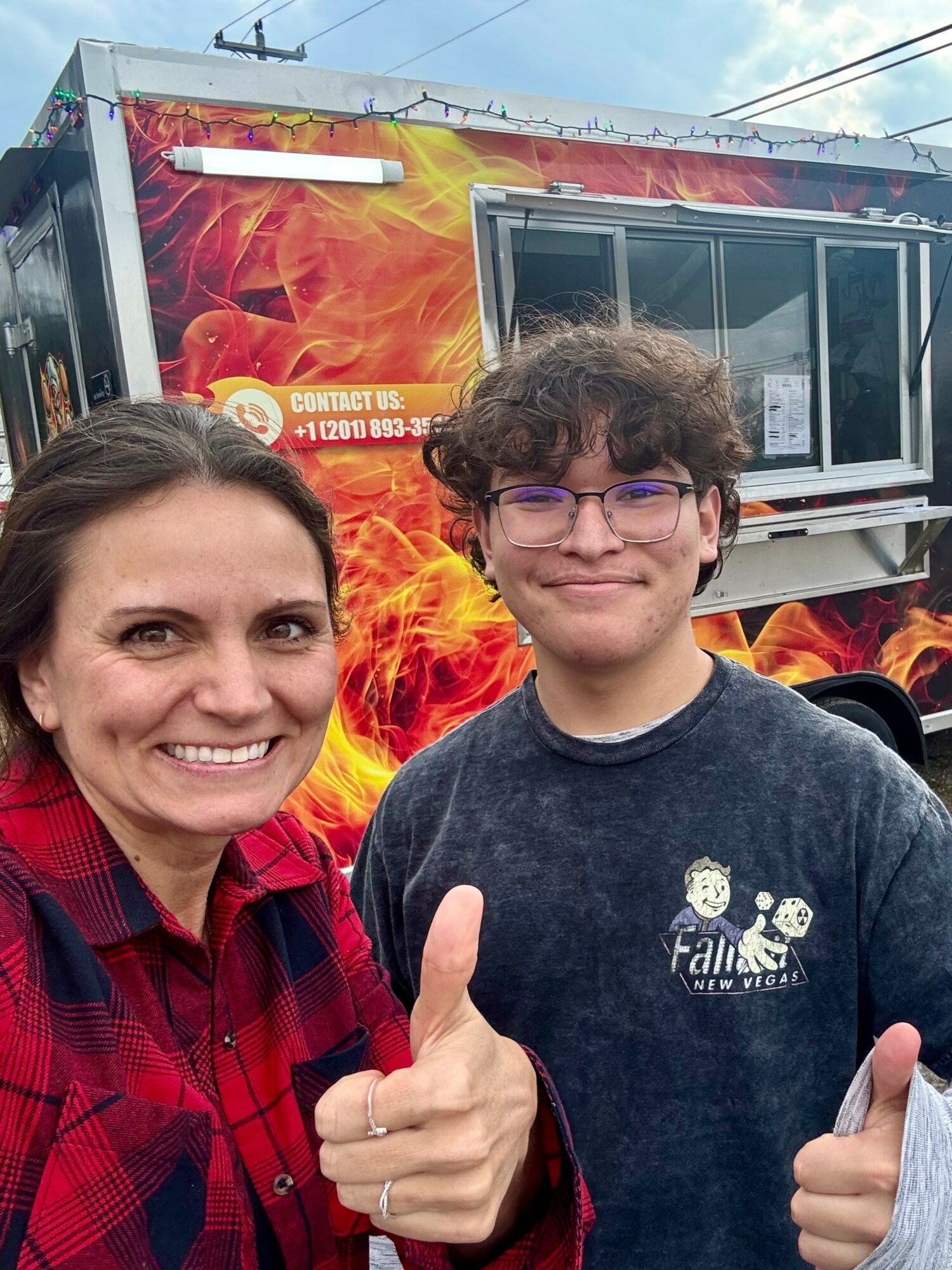 Woman and young person smiling and giving thumbs-up in front of a fire-themed food truck.