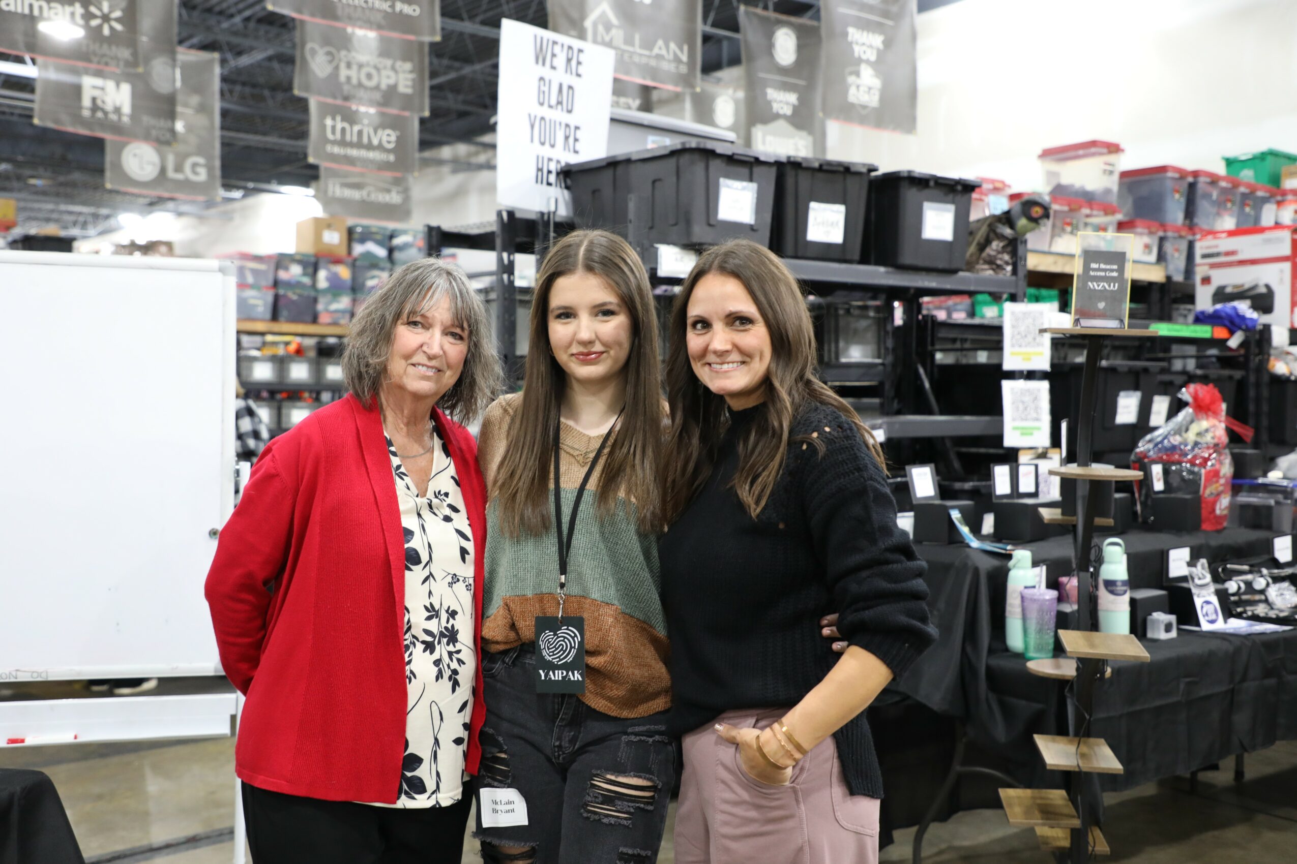 Three women standing together in a store, smiling, with shelves and products in the background.