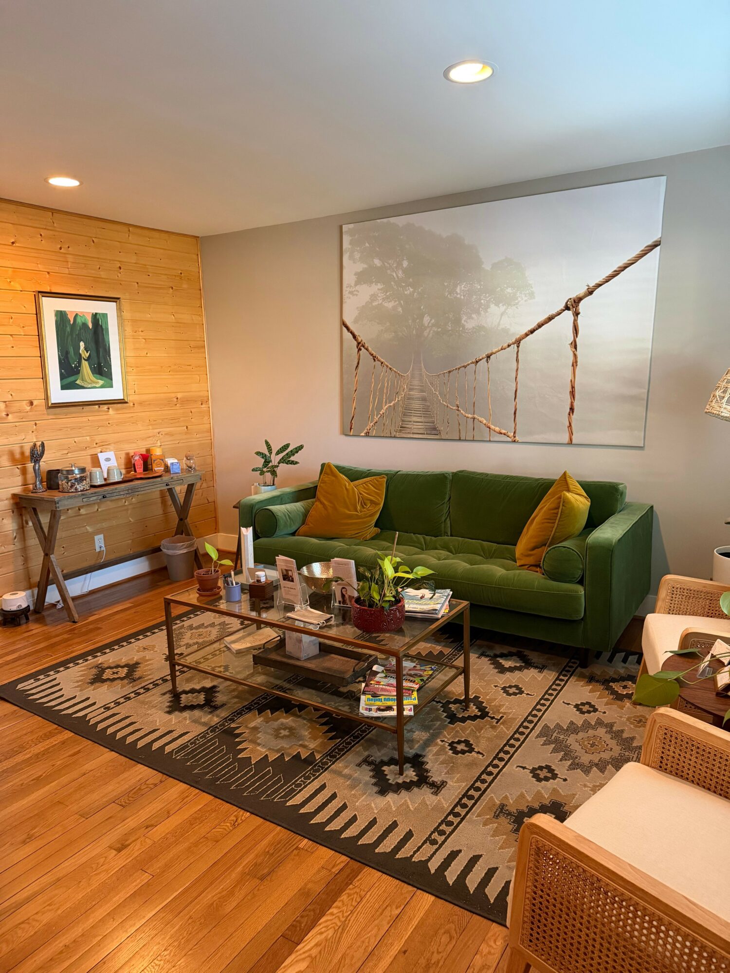 Living room with green sofa, wooden side table, coffee table, and large wall art of a bridge with trees.