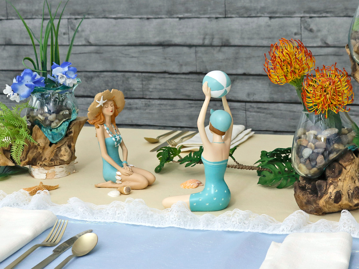 Decorative scene with a mermaid figurine, two children with beach balls, flowers, and a wooden background.