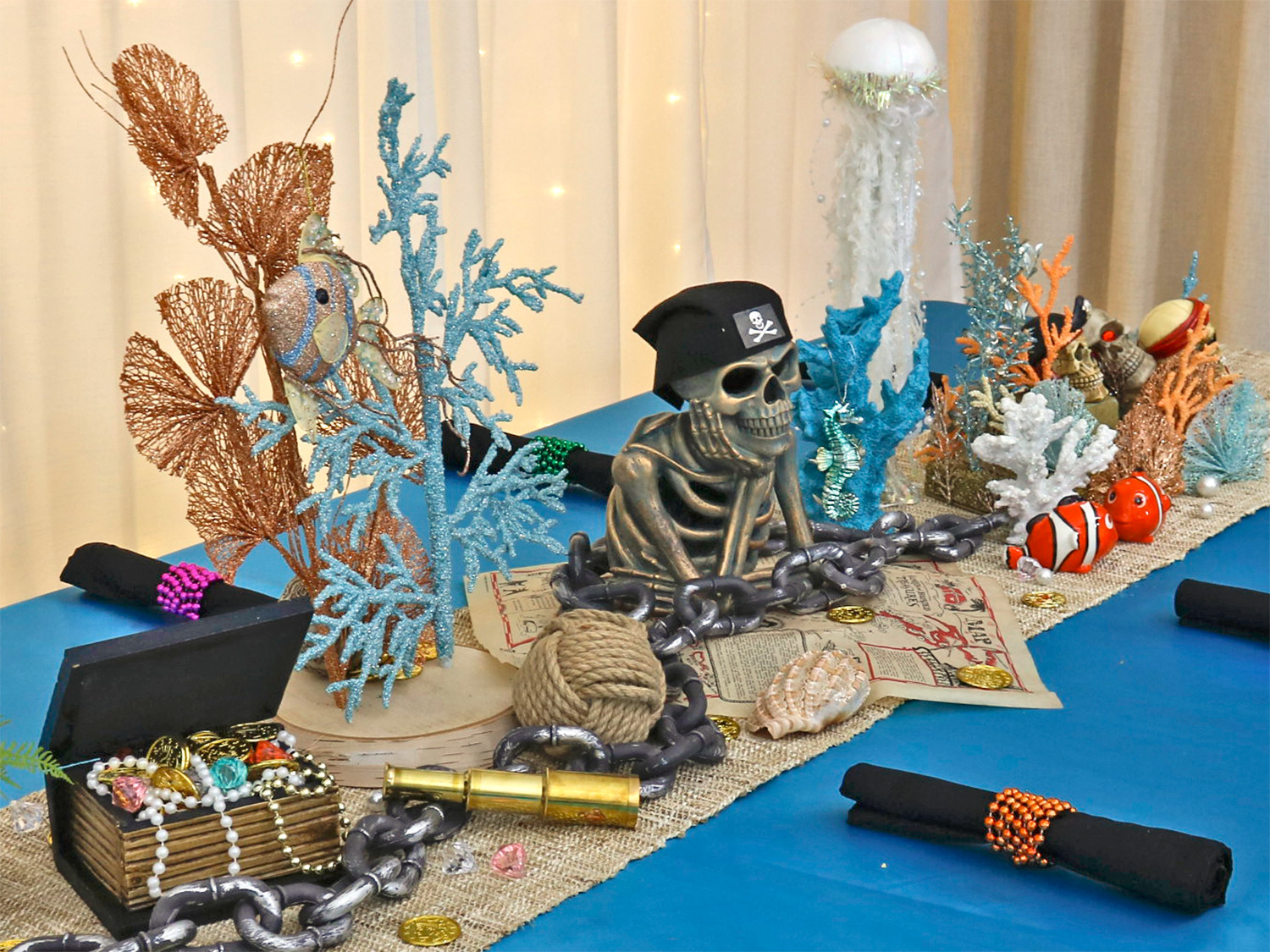 Decorative skeleton figure with ocean-themed ornaments on a table, including coral, fish, and a treasure chest, with a blue tablecloth.