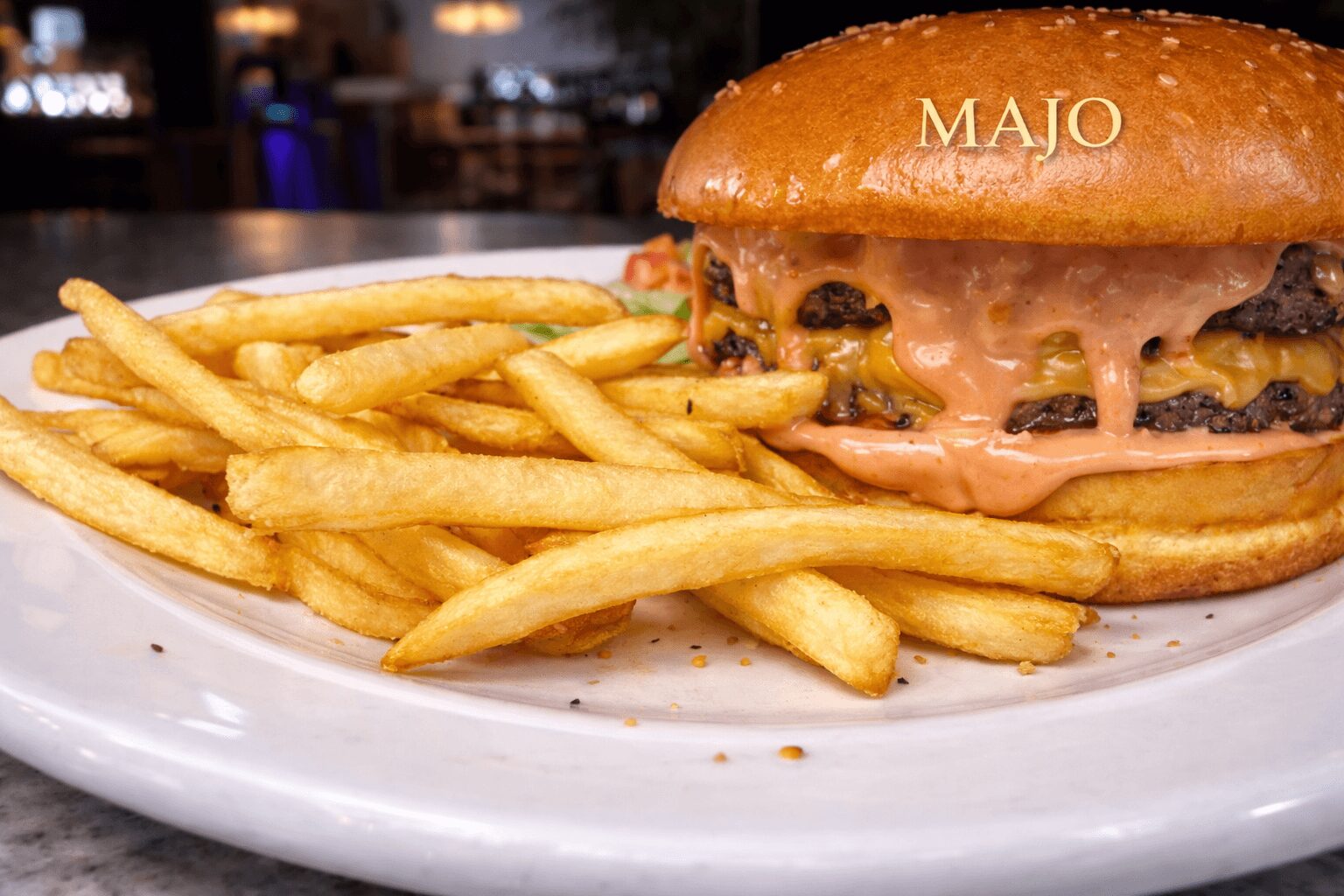 Burger with cheese, lettuce, and sauce next to a pile of French fries on a white plate.