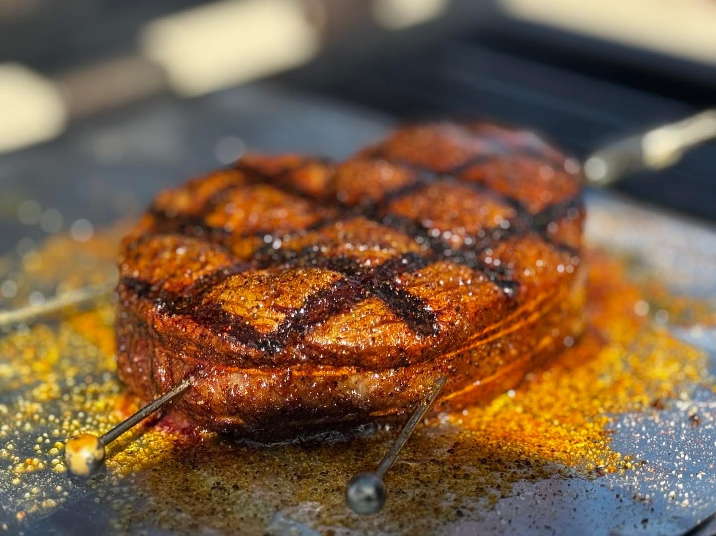 Grilled meat with grill marks resting on a surface with spices and juices around it.