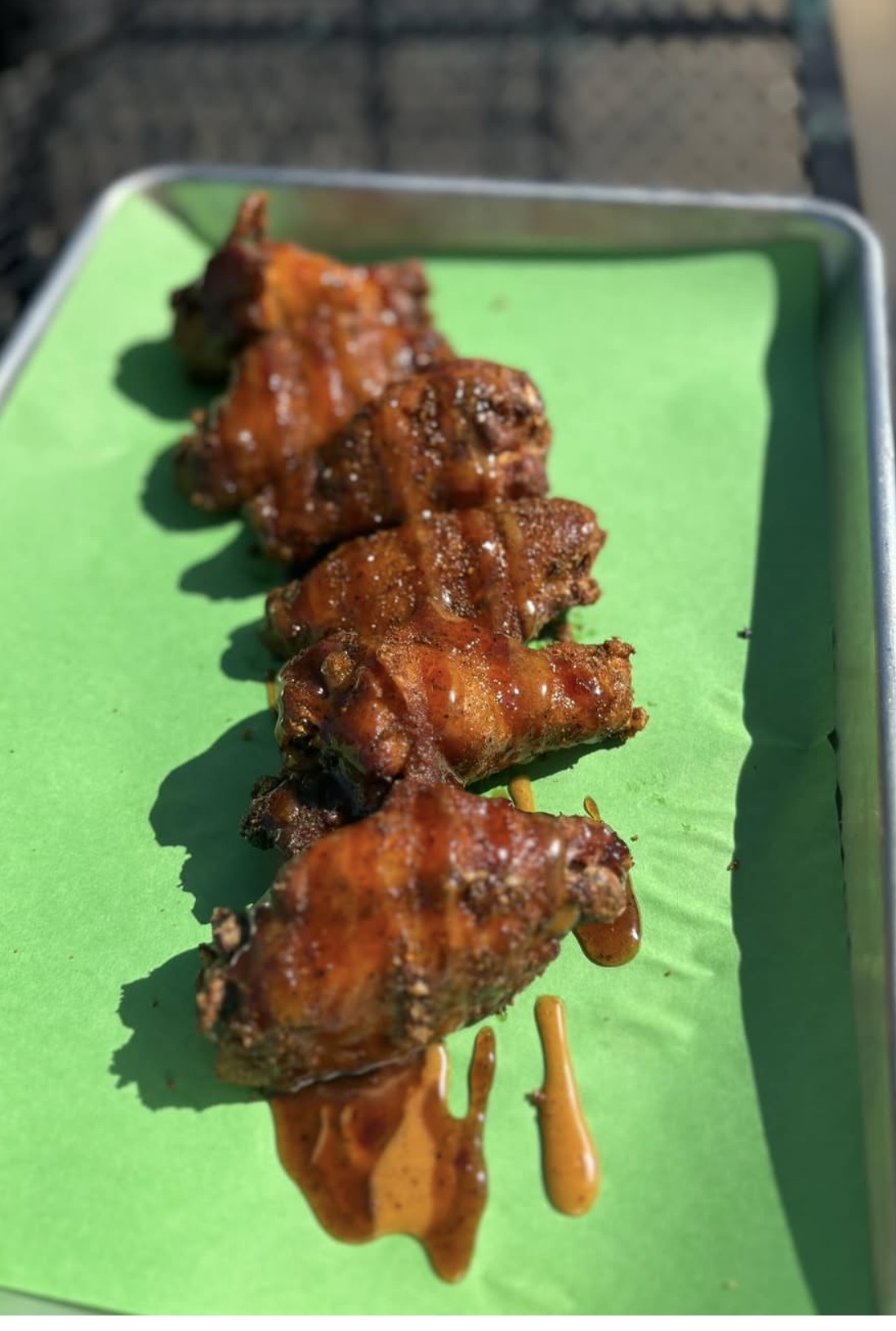 Skewered grilled meat with sauce on green paper, on a metal tray.
