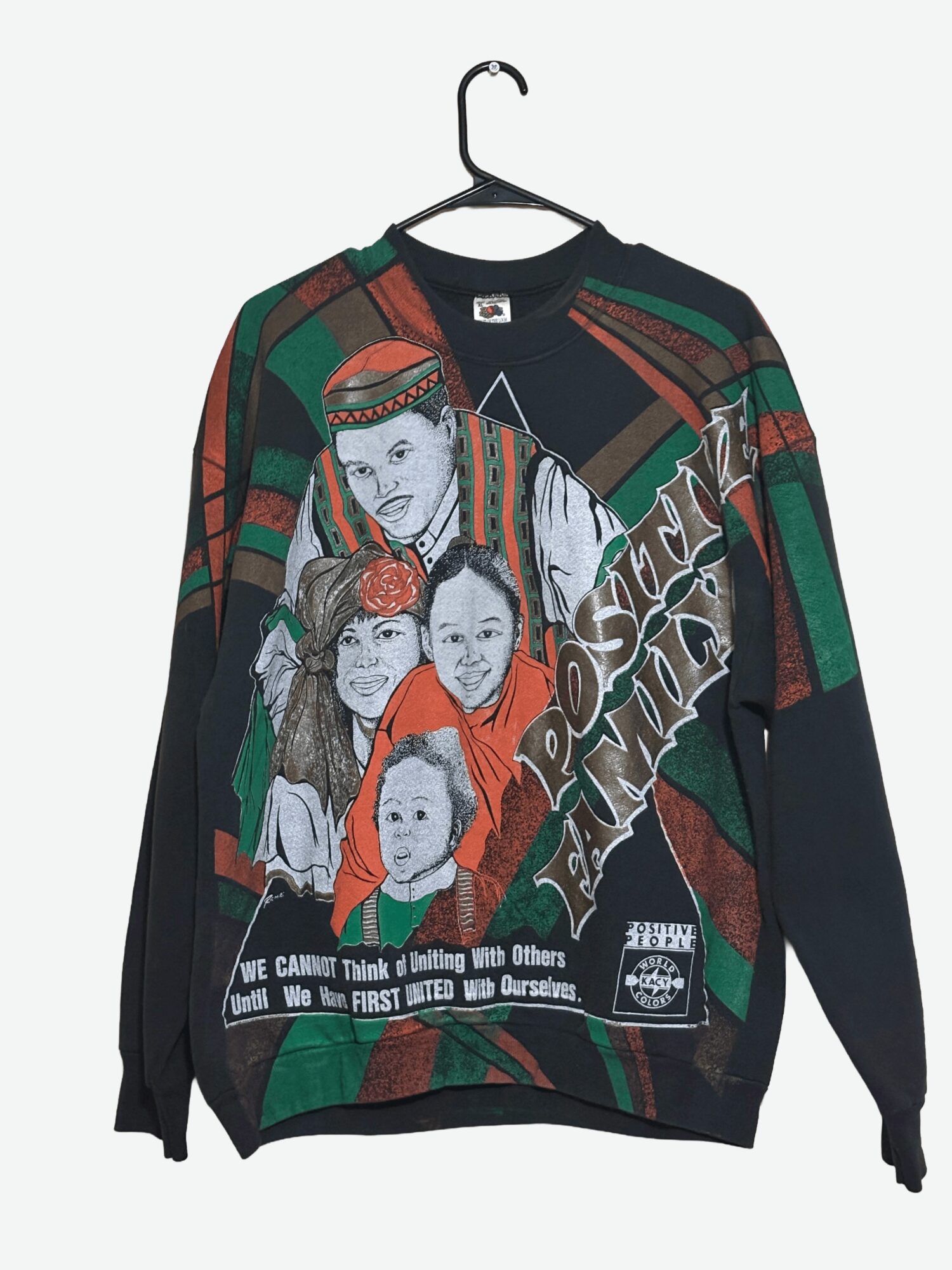 Sweater with colorful abstract patterns and portraits of children, hanging on a black hanger against a light background.