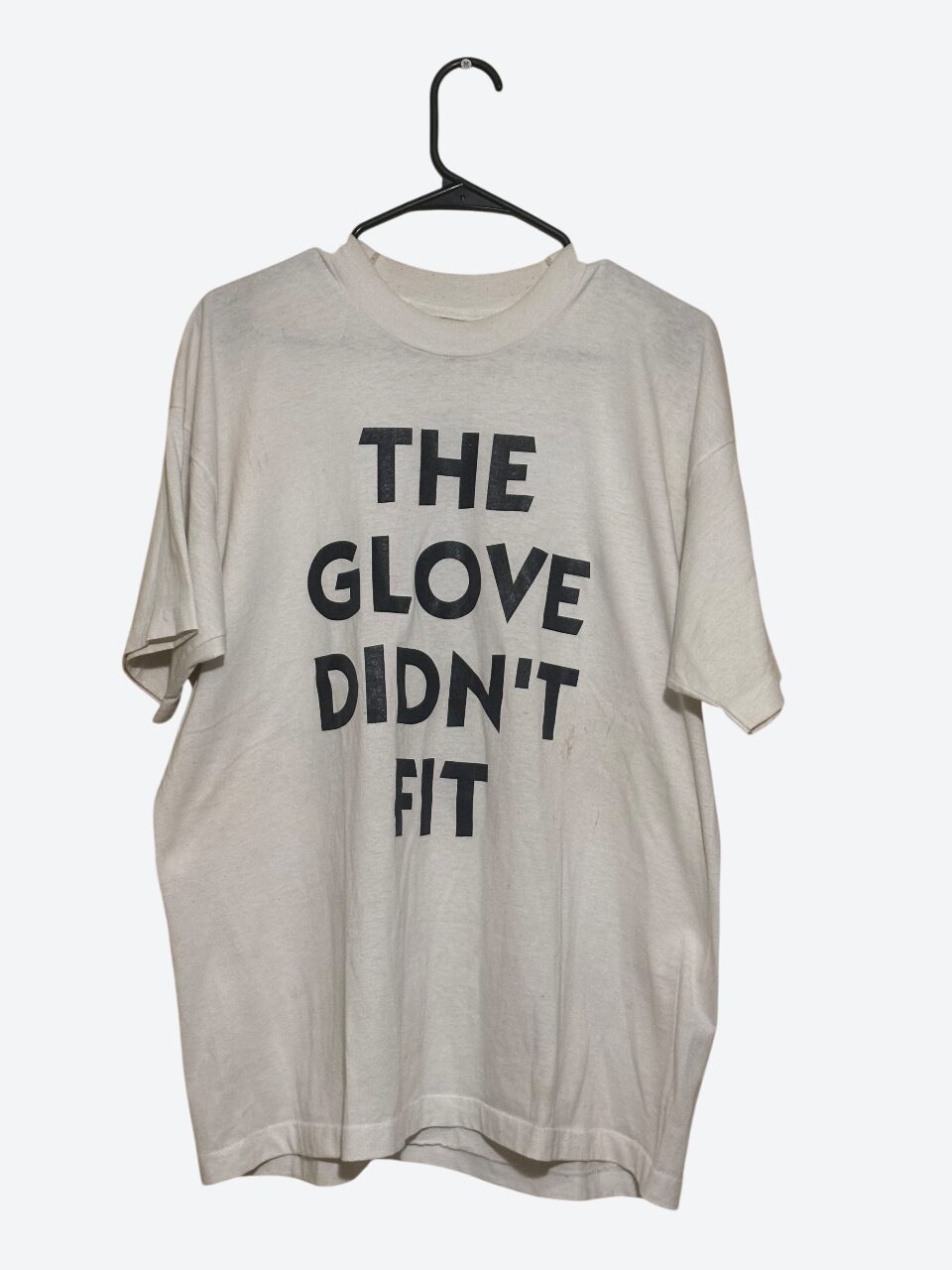 Loose beige T-shirt with black text hanging on a black hanger against a plain background.