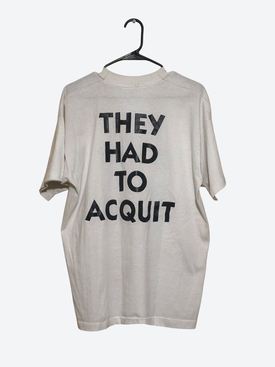 Light-colored oversized T-shirt with bold black text reading 'THEY HAD TO ACQUIT' on front, hanging on a black hanger.