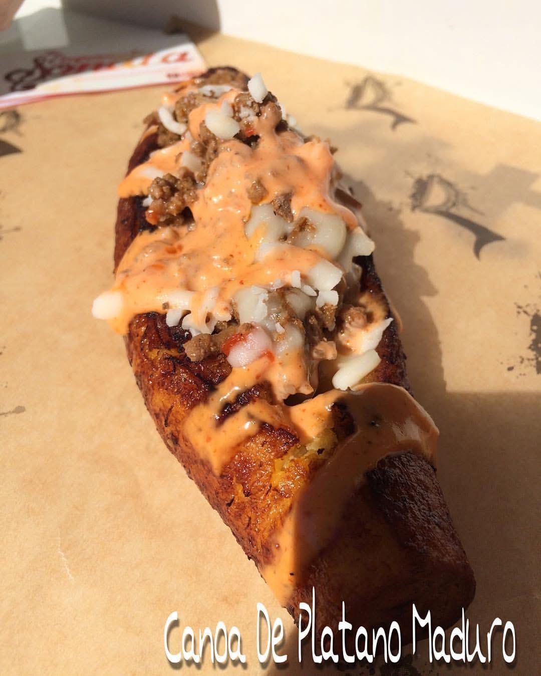 Fried plantain topped with cheese, sauce, and crunchy toppings on parchment paper.