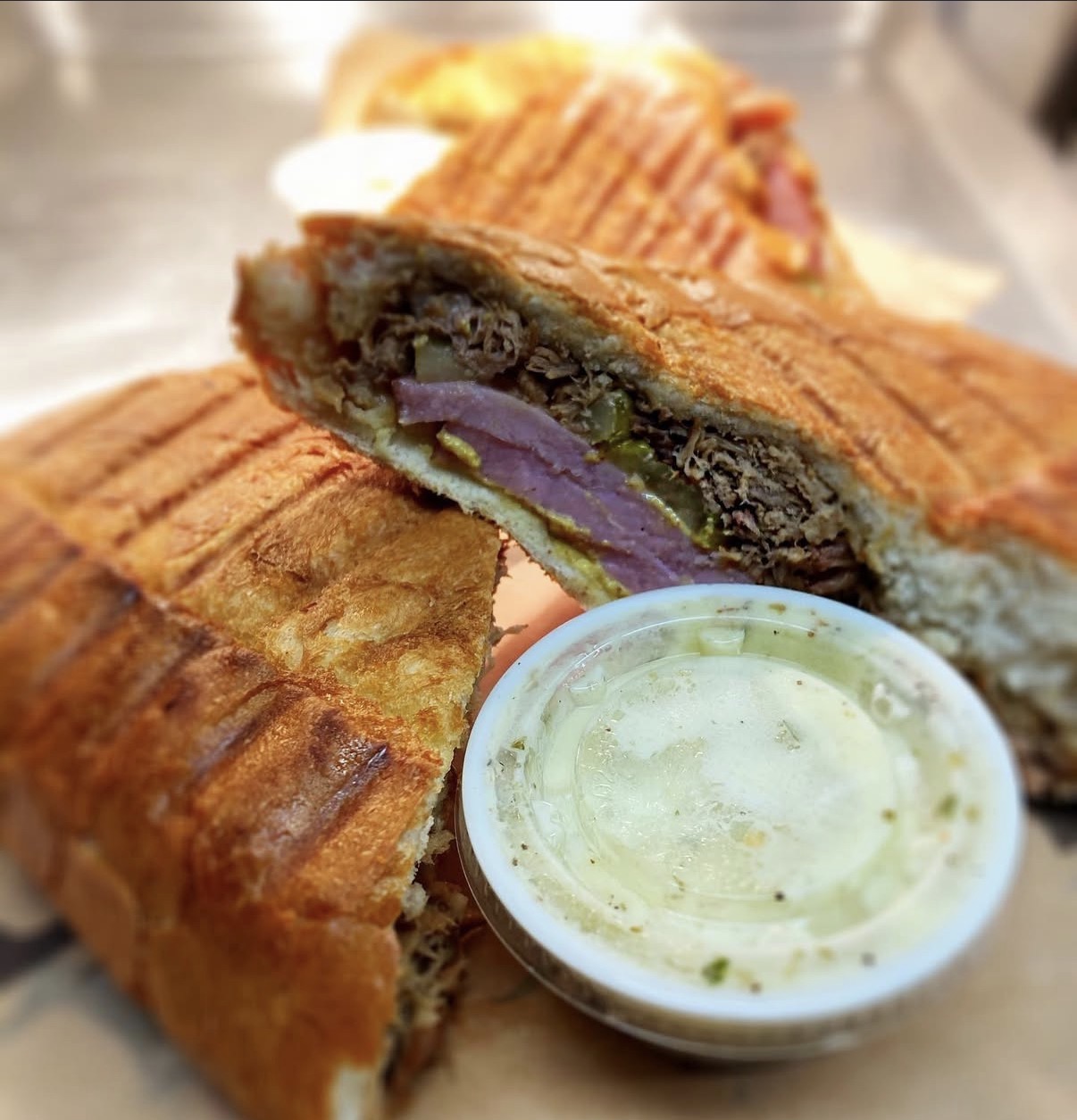 Close-up of a toasted sandwich with purple filling, served with a small bowl of green dipping sauce.