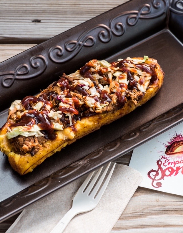 Banana split topped with chocolate syrup, nuts, and coconut on a black tray, with a fork and a paper napkin nearby.