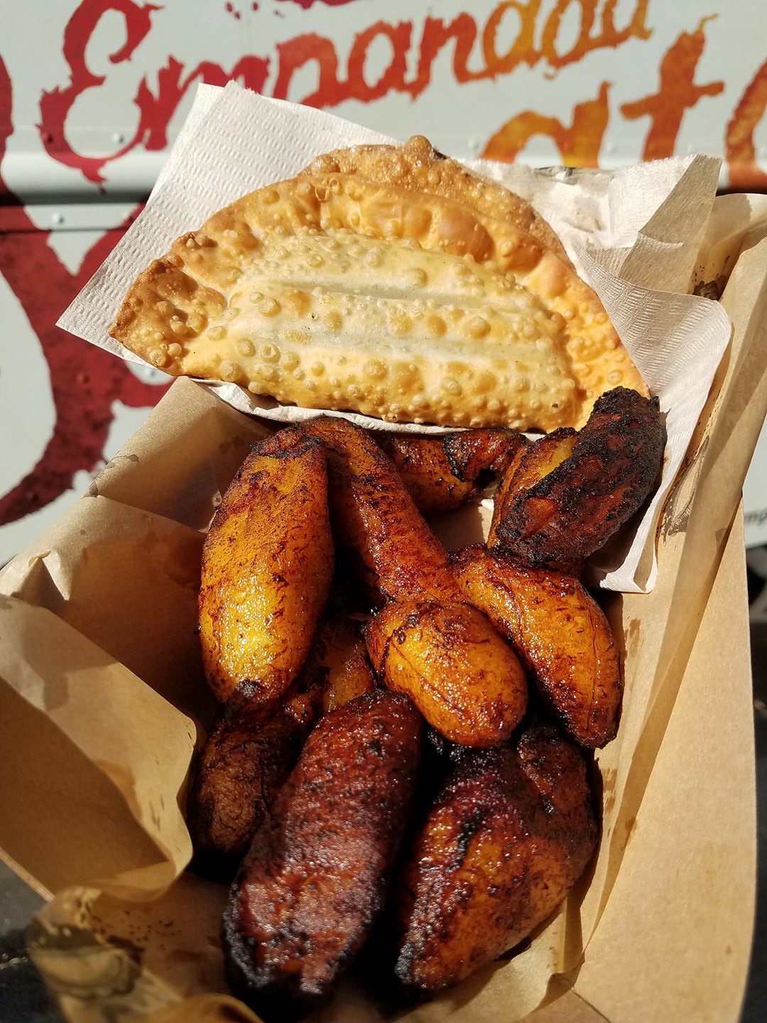 Basket of fried plantains with a slice of cheese bread on top, in a paper-lined container.