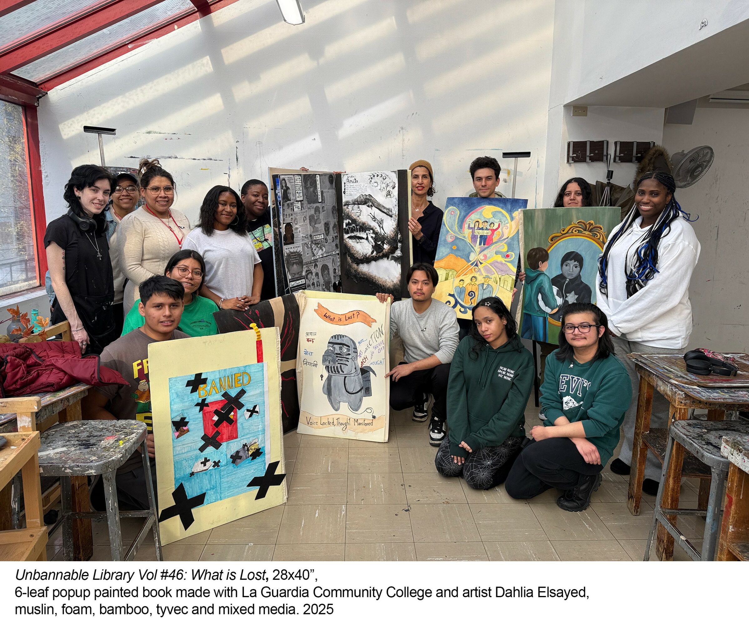 Group of people displaying colorful paintings in an indoor space with white walls and natural light.