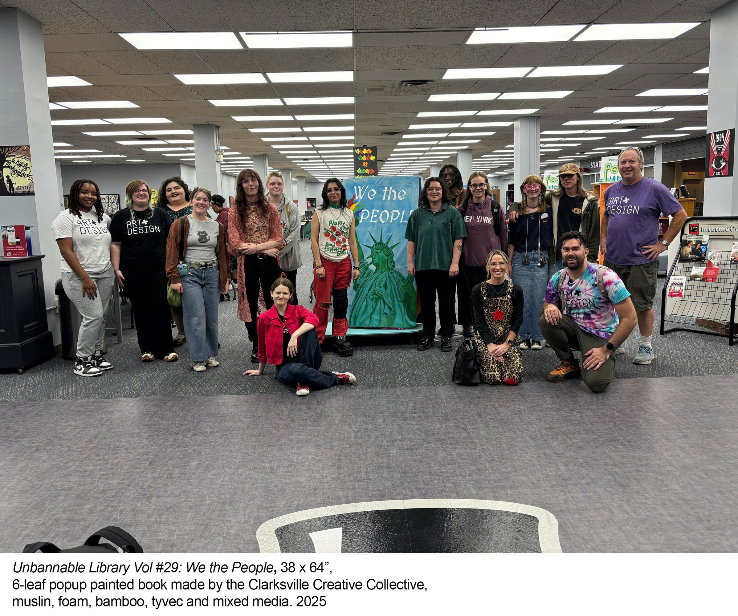 Group of people standing and sitting in a large indoor space with a banner behind them.