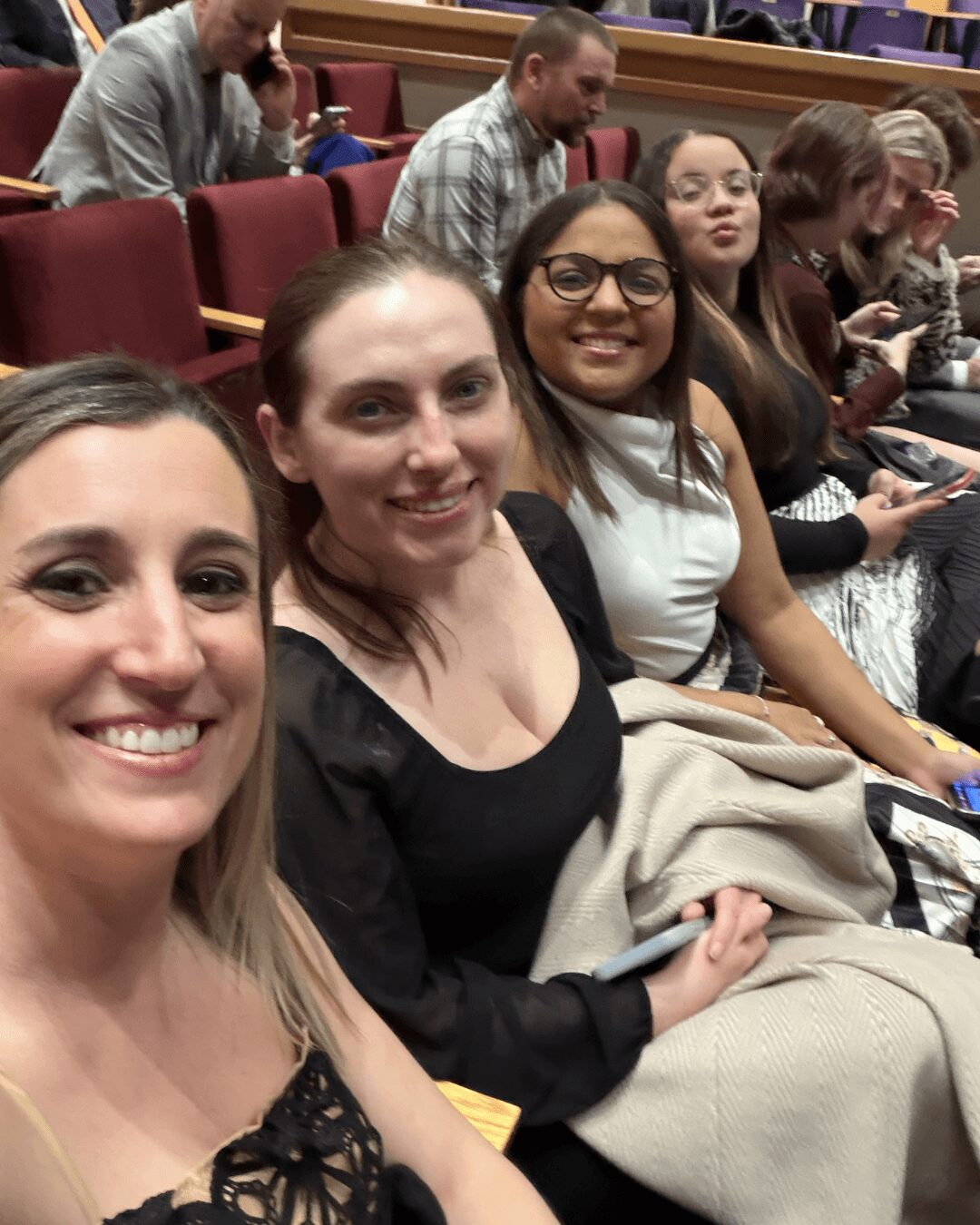 Four women sitting in a row at an event, smiling and looking at the camera.