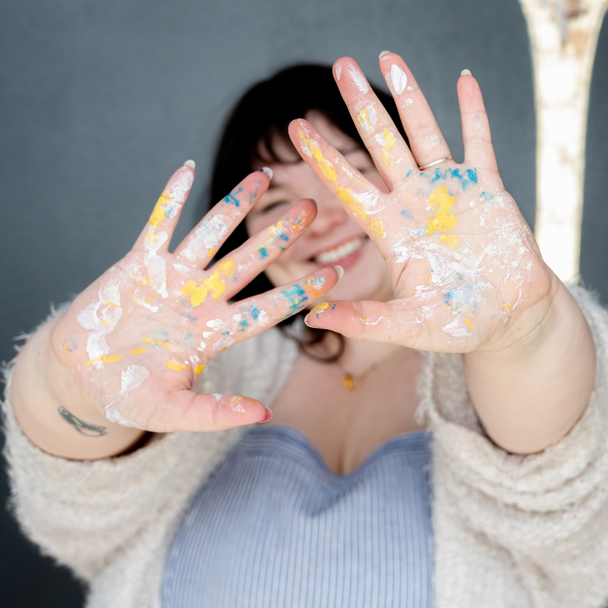 Person with paint-covered hands smiling, hands raised towards camera, background blurred.