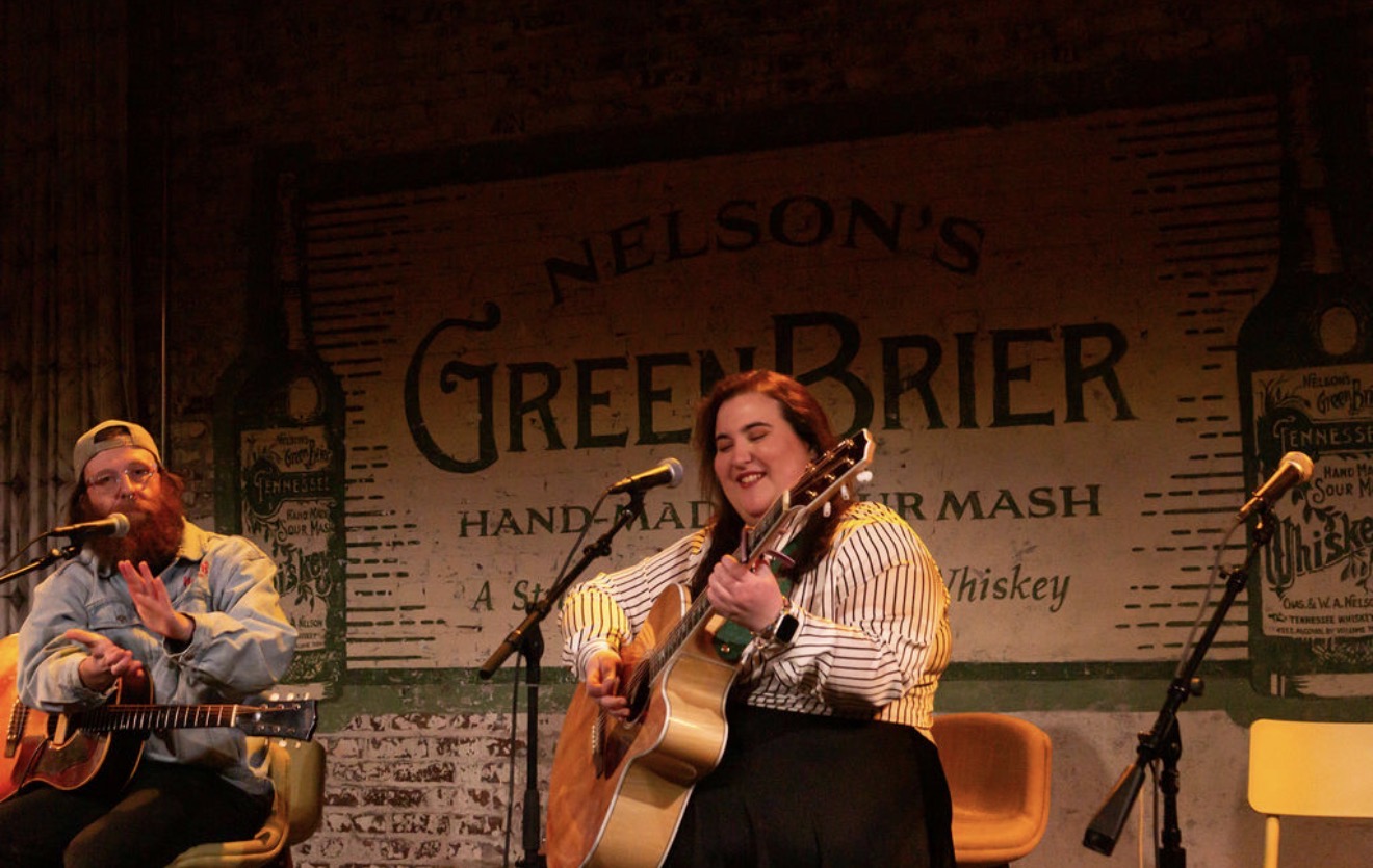 Two women playing guitars on stage with a large Nelson's Green Brier sign in the background.