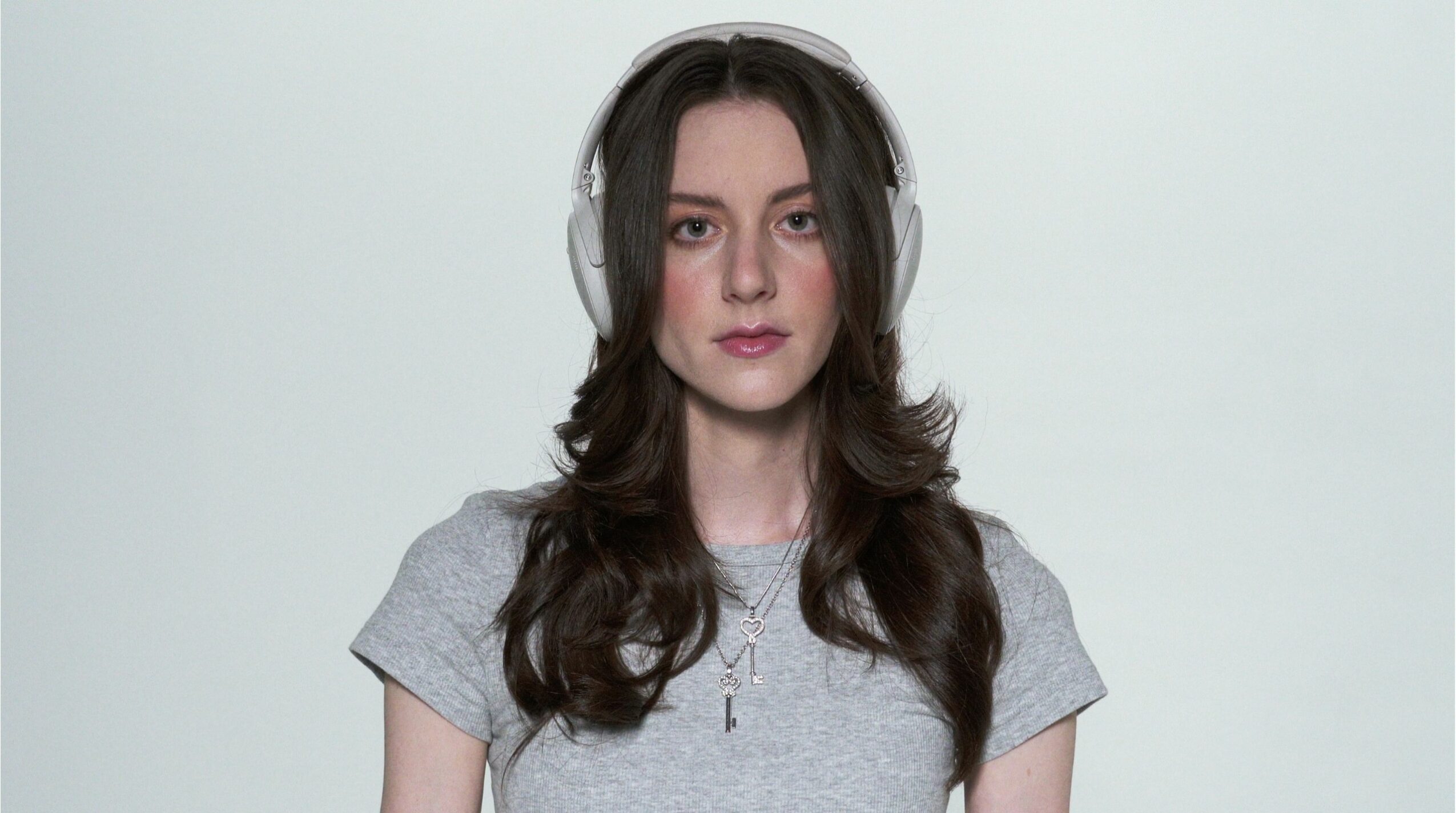 Young woman with long dark hair wearing headphones and a gray t-shirt, facing forward.