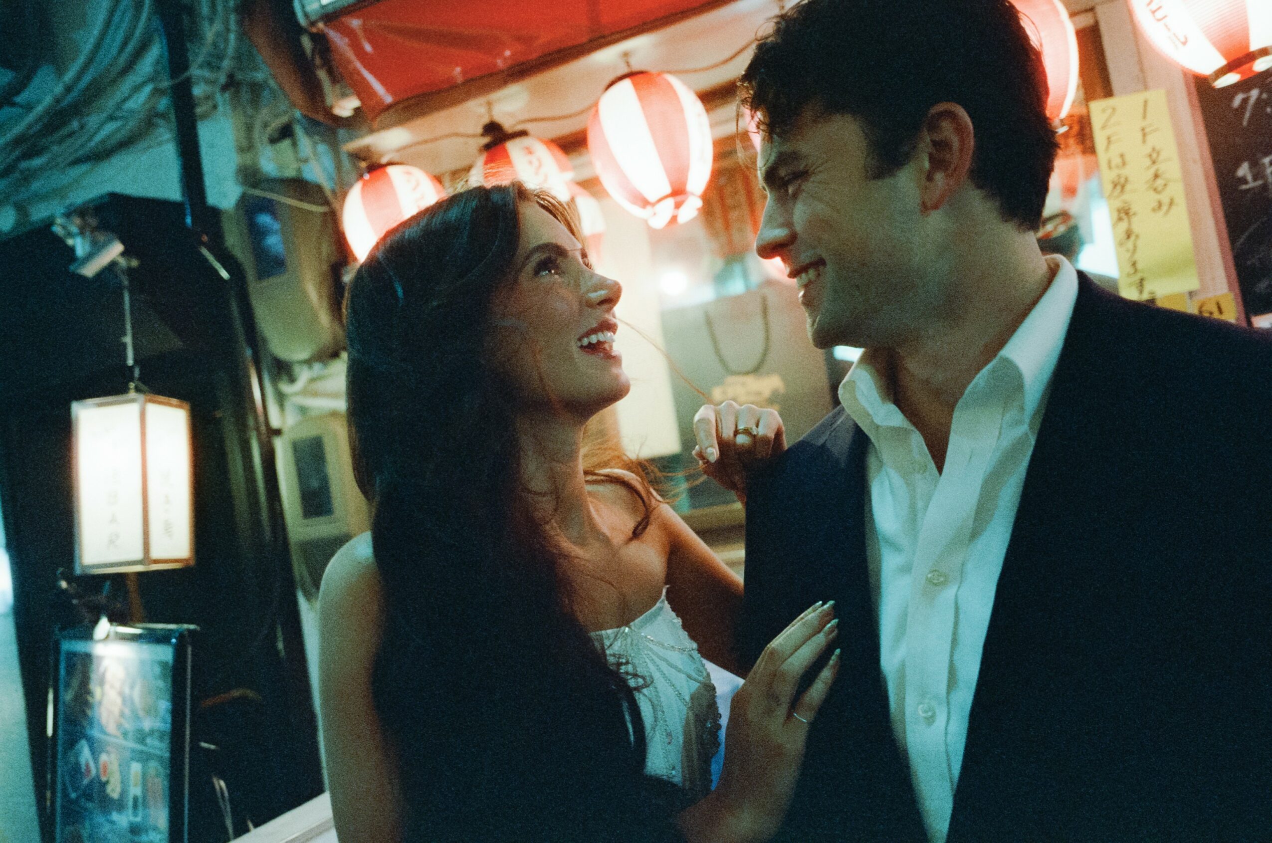 A woman and a man smile at each other in a festive setting with lanterns and lights.