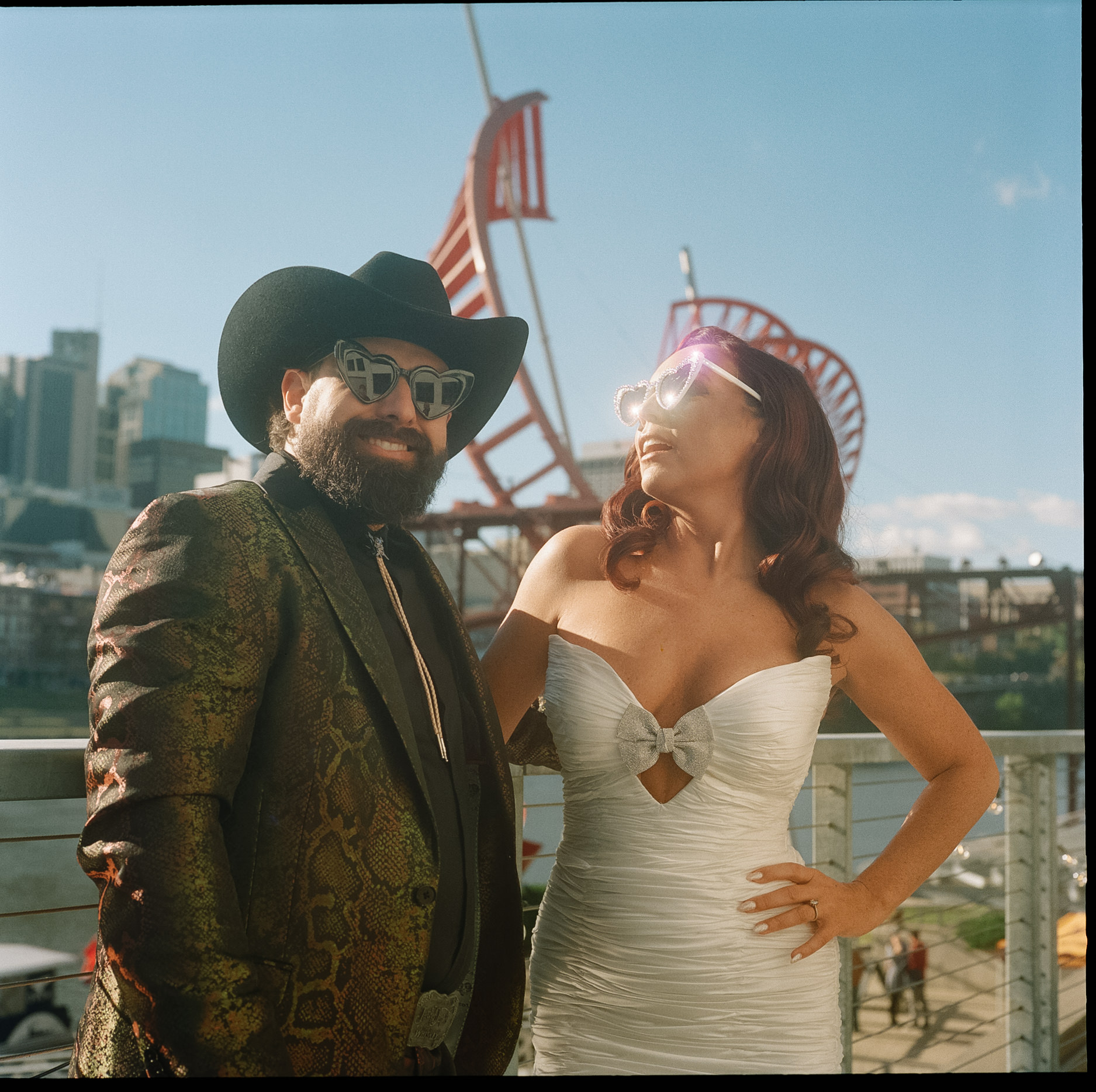 Man and woman posing outdoors with city skyline and amusement park rides in background.