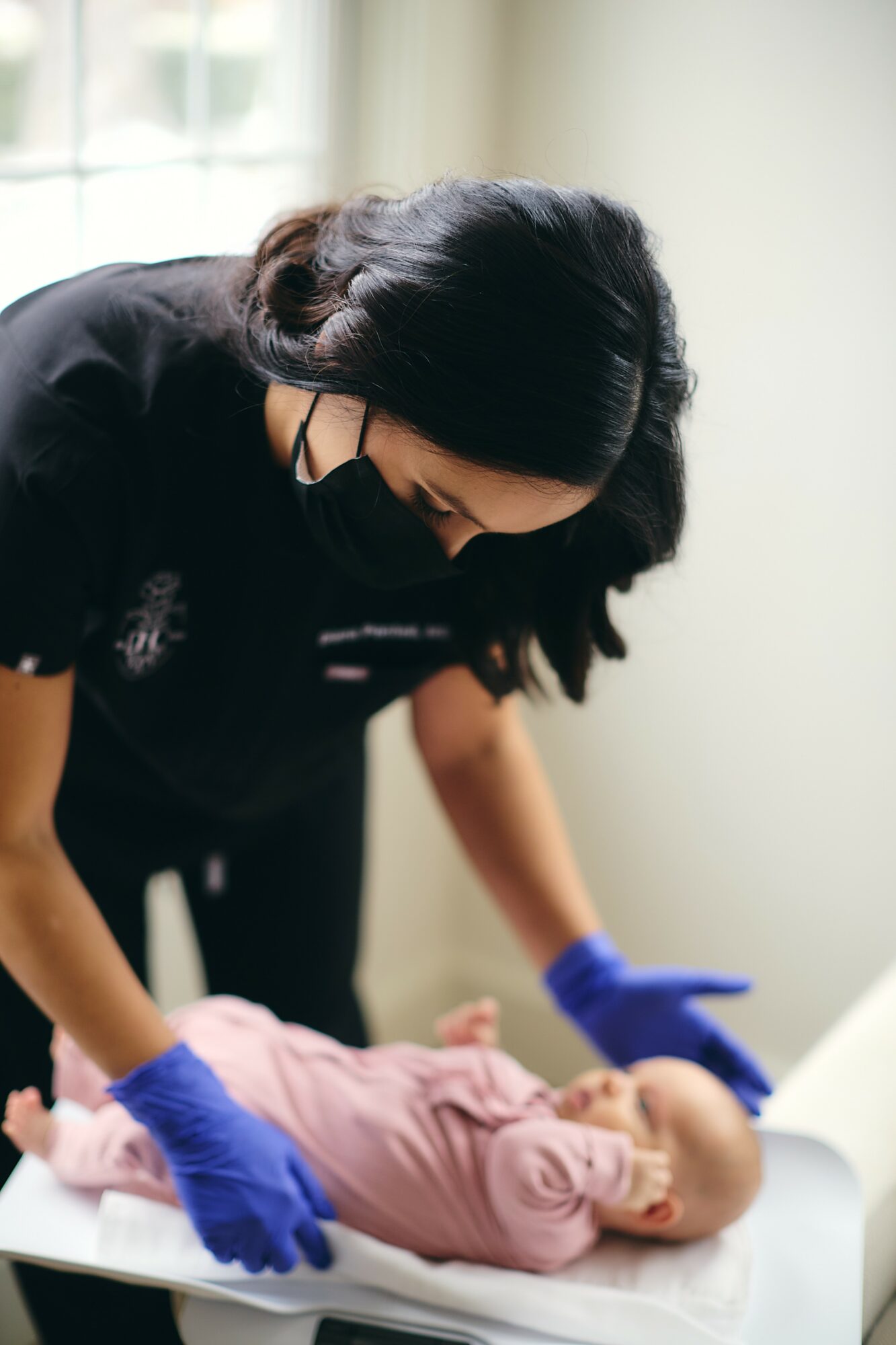 Woman wearing gloves leaning over a baby lying on a table indoors.