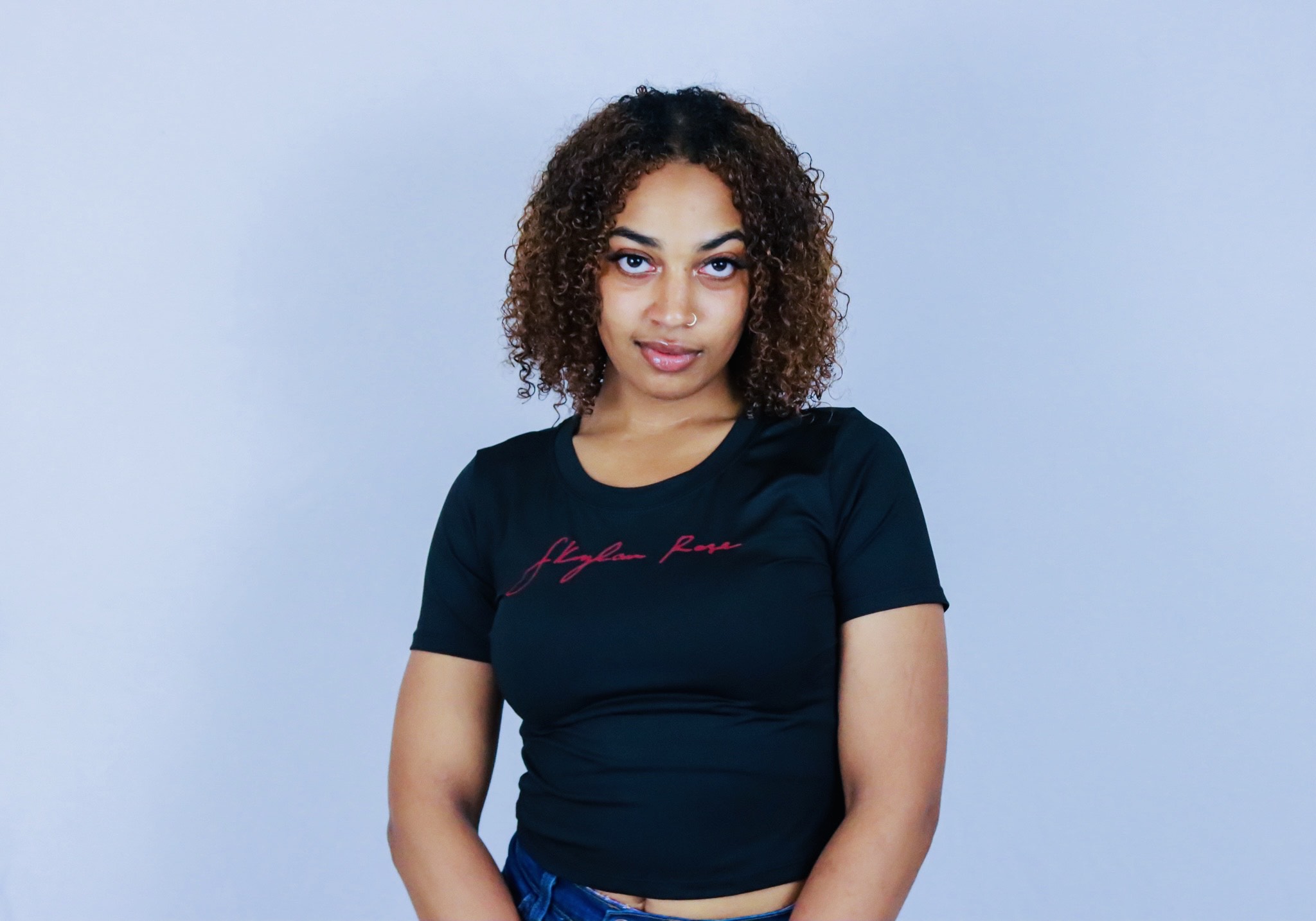 Young woman with curly hair wearing a black T-shirt against a light blue background.