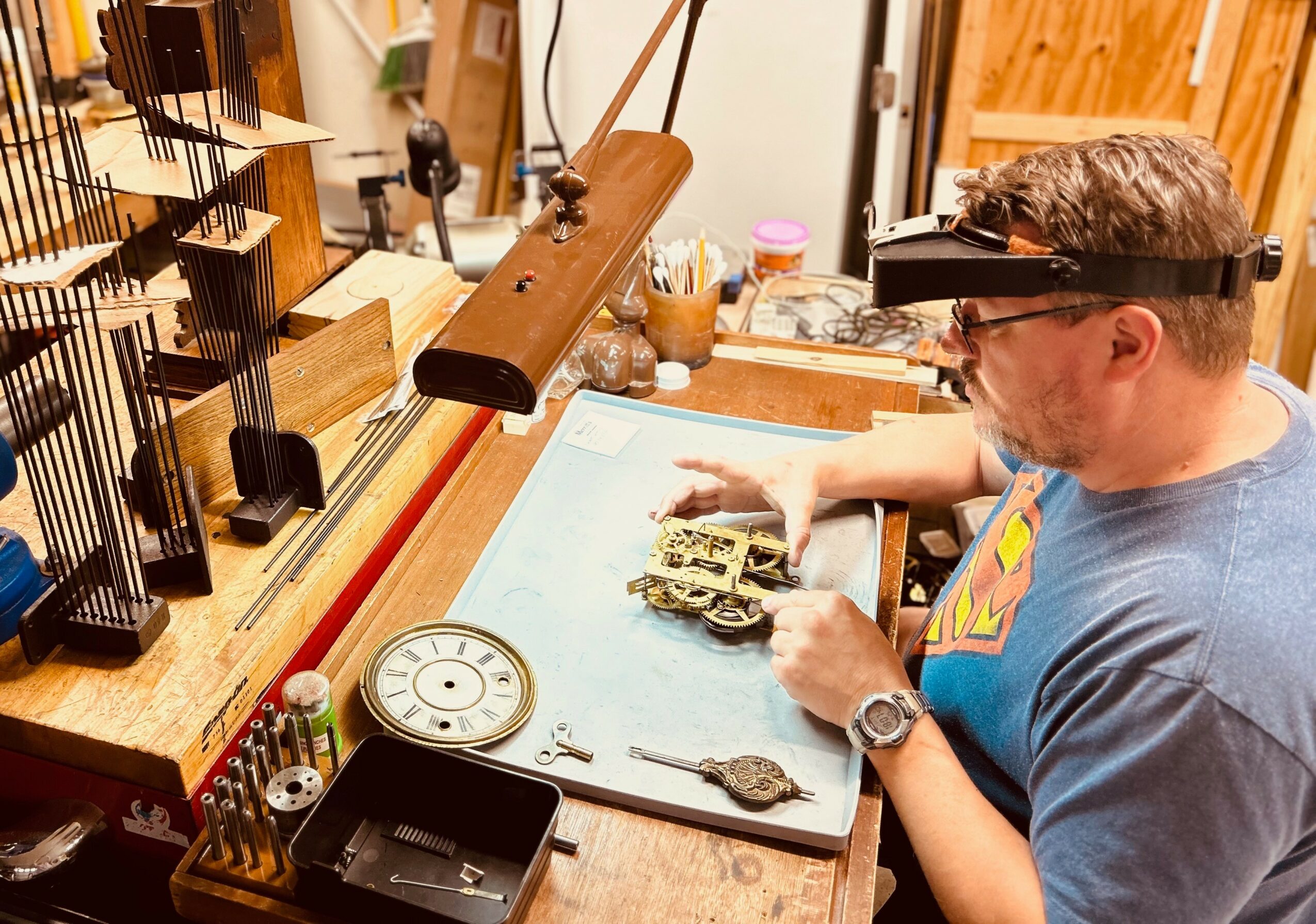 Person wearing magnifying glasses working on a small object at a workbench with tools and equipment.