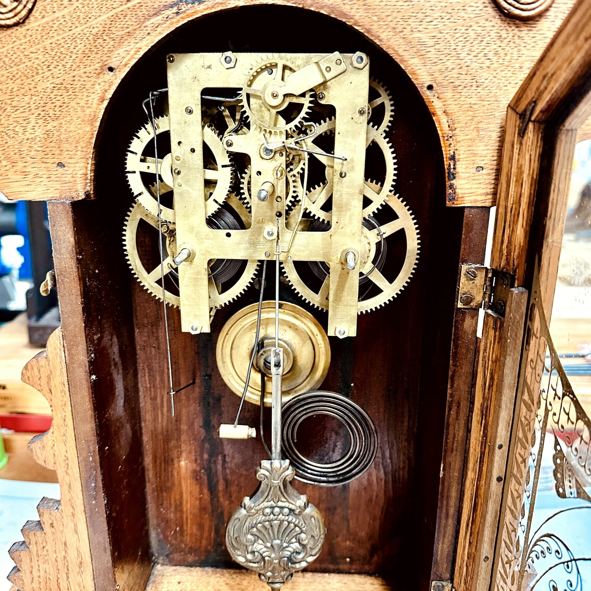 Close-up of clock mechanism with gears and pendulum inside wooden case, with open door showing internal parts.