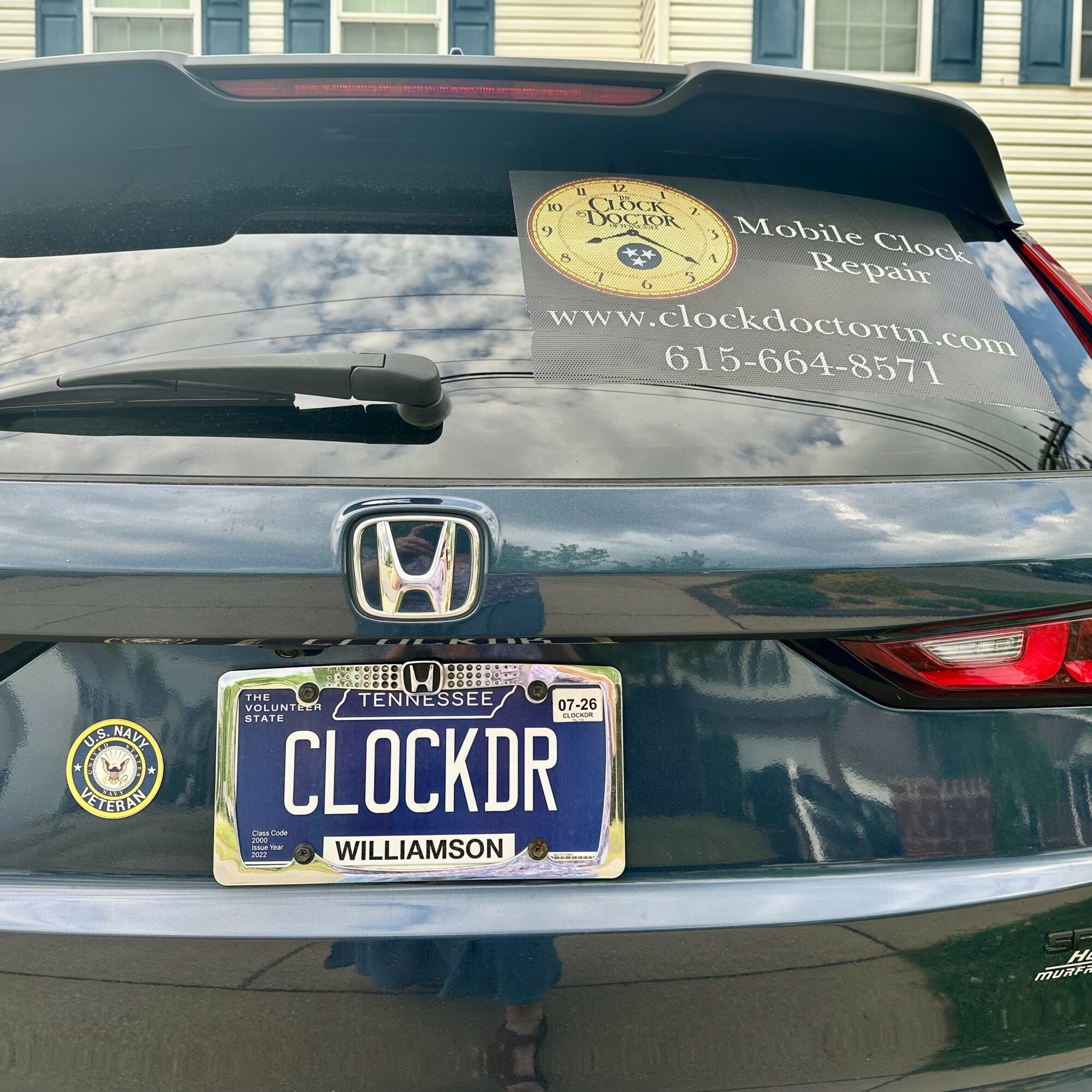 Back of a dark-colored Honda vehicle with Tennessee license plate reading 'CLOCKDR' and a sticker for clock repair service on the rear window.