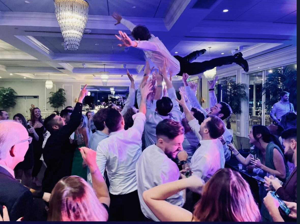 People dancing and lifting a person in a decorated indoor venue with chandeliers and large windows.